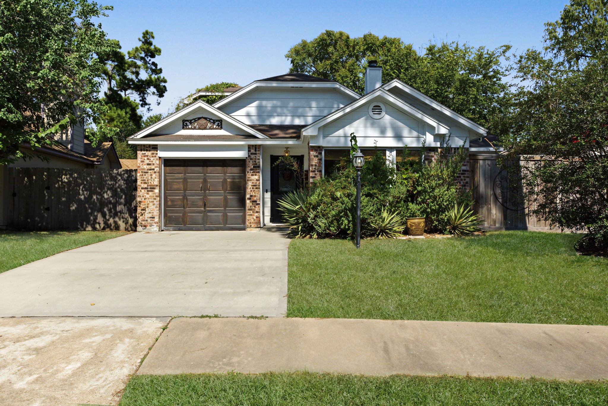 Charming brick and white siding exterior framed by mature trees, a lamp post and lush landscaping!