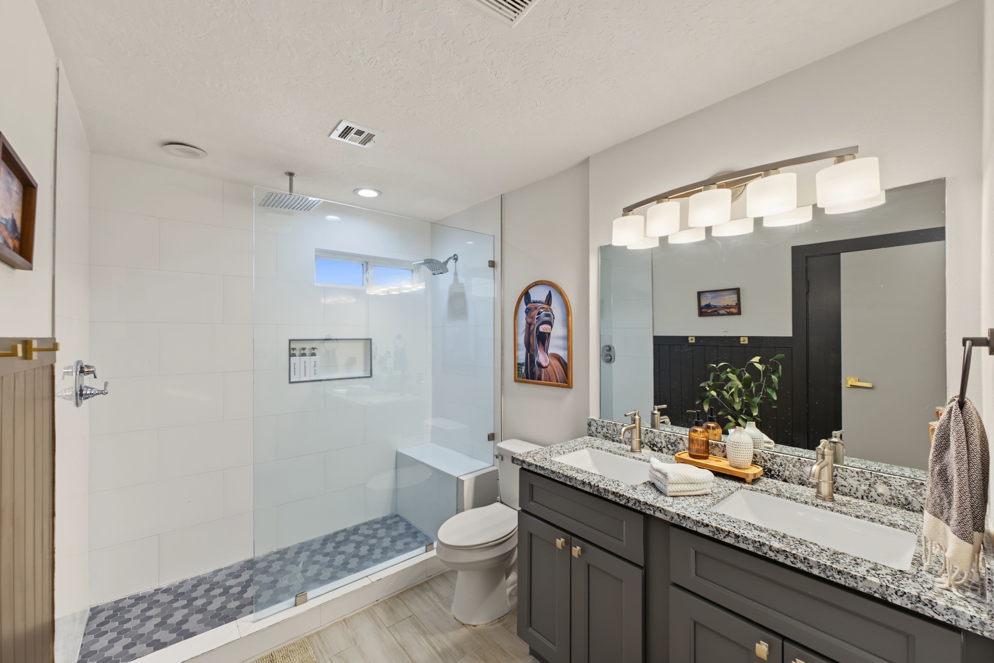 Remodeled bath boasts a walk-in shower with frameless glass, rain head, hex mosaic floor, built-in bench and niche, plus a granite double vanity!