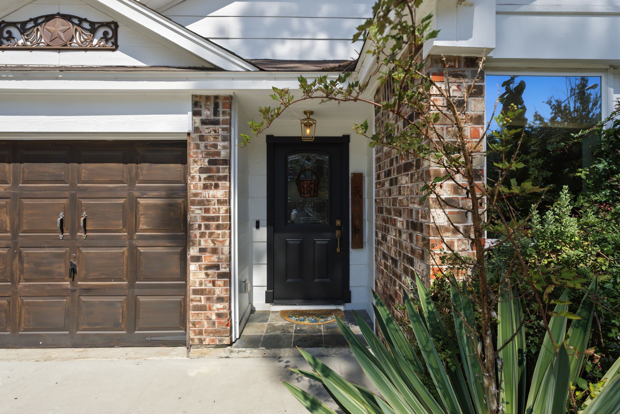 Welcoming entry features a black front door with leaded glass, slate tile stoop and lantern lighting.