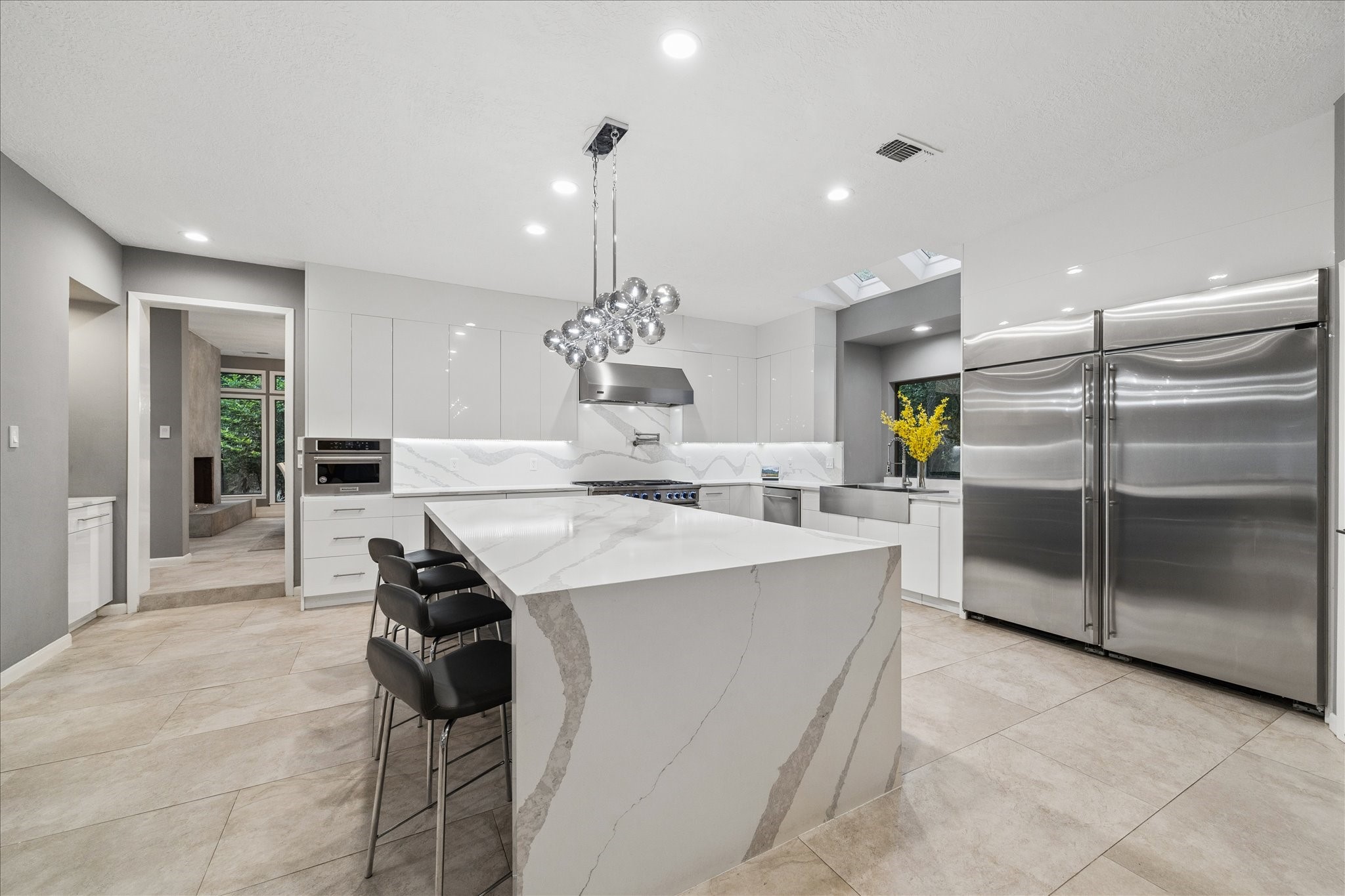 The chef's kitchen features sleek white cabinetry, a large marble island with seating, and stainless steel appliances. The open layout is enhanced by bright lighting and a stylish, contemporary design, perfect for entertaining and everyday living.