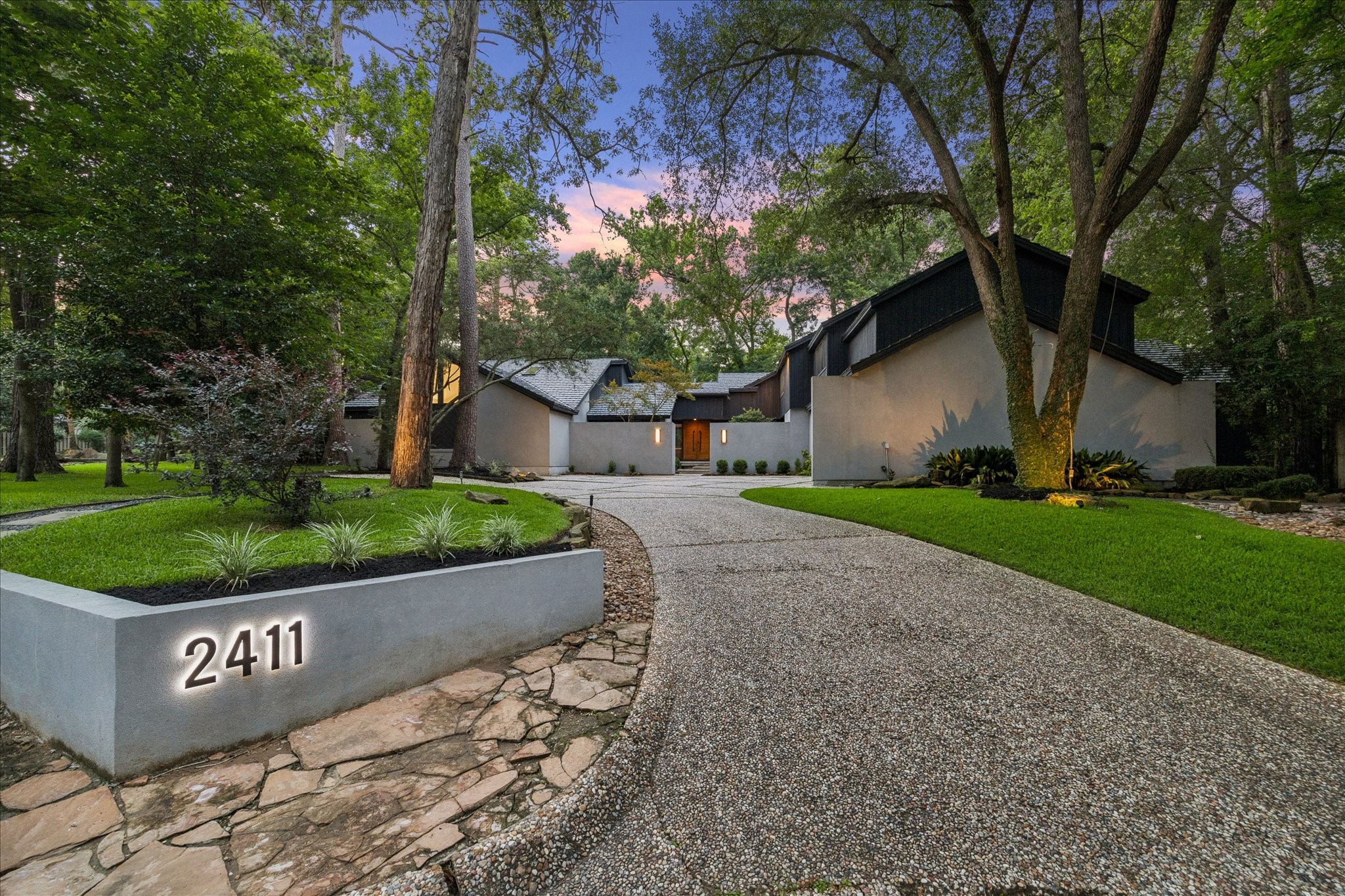 Welcome to Oakbank Estate, nestled among mature trees. The property features a curved driveway leading to the entrance, well-maintained landscaping, and a prominent address marker. The setting is serene and private, ideal for a peaceful living environment.