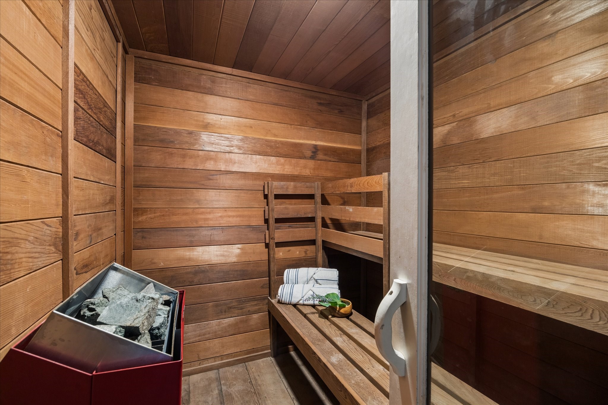 Your very own wood-paneled sauna with a bench and a rock heater, perfect for relaxation and wellness at home.