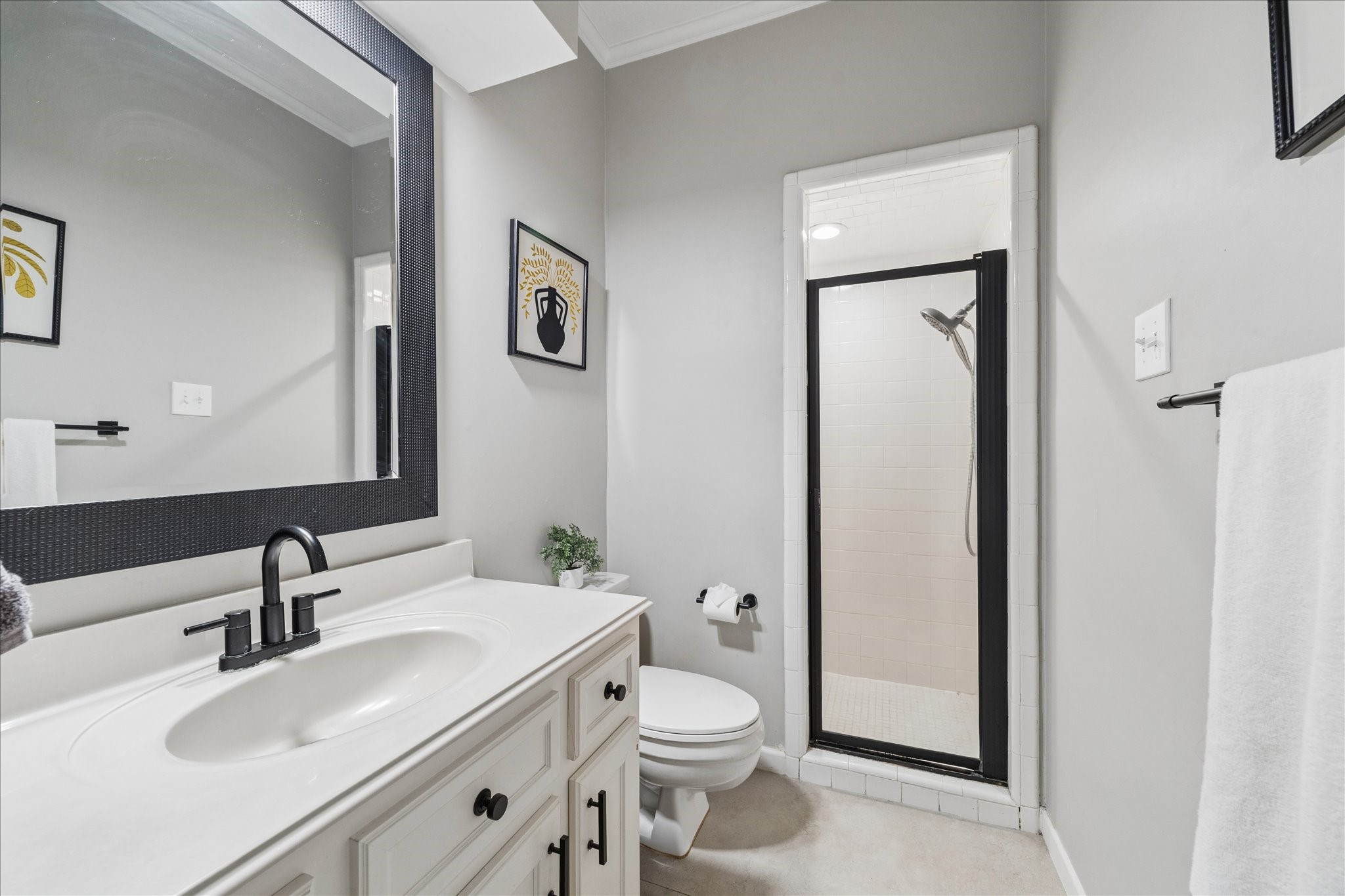 This bathroom is adjacent to the guest bedroom and features a sleek design with a modern vanity, a large framed mirror, and a walk-in shower with a glass door. Neutral tones create a clean, inviting atmosphere.
