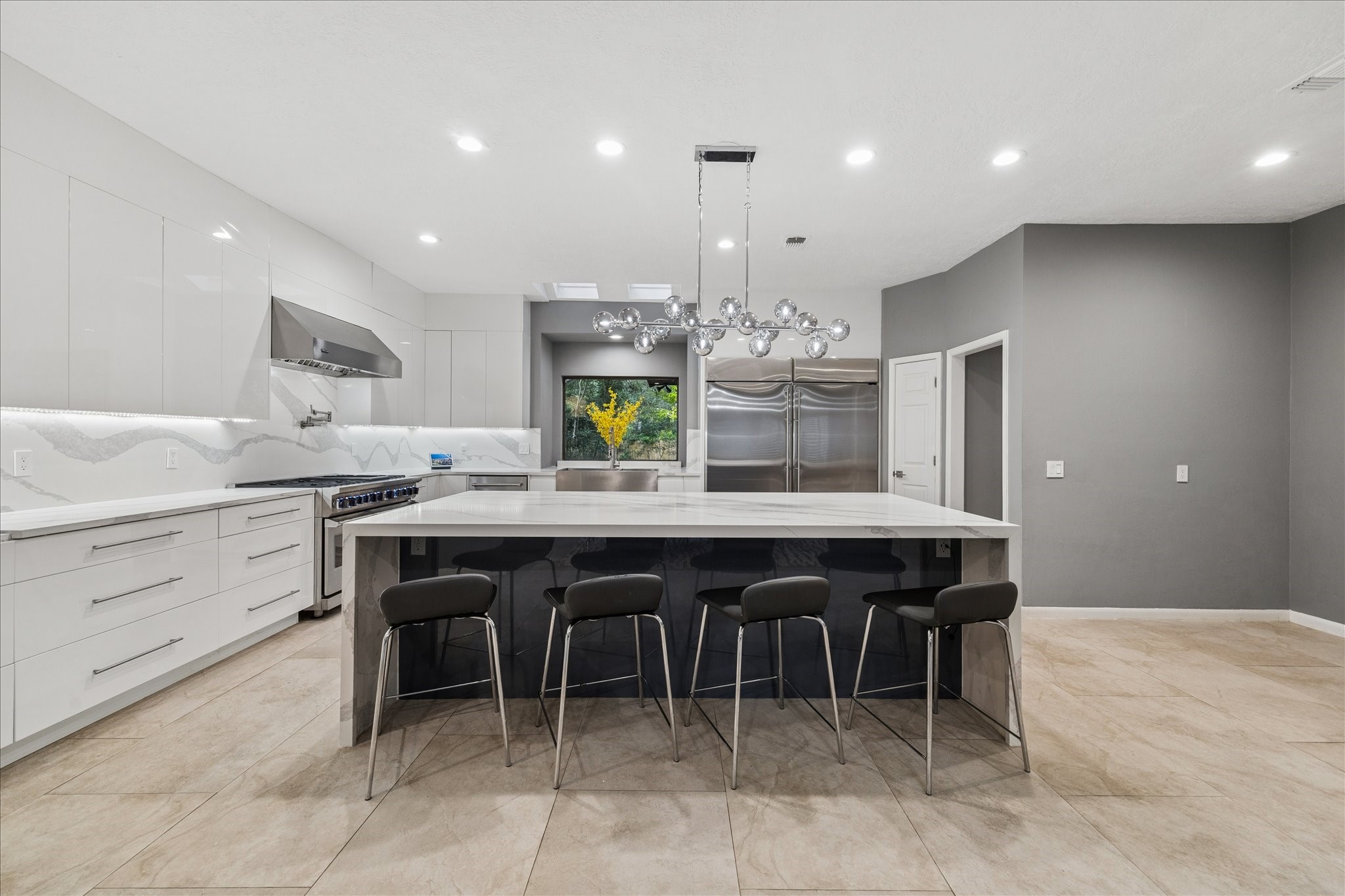 Spacious modern kitchen with sleek white cabinetry, a large island with seating, stainless steel appliances, and contemporary lighting. Ideal for cooking and entertaining. Spacious modern kitchen with sleek white cabinetry, a large island with seating, stainless steel appliances, and contemporary lighting. Ideal for cooking and entertaining.