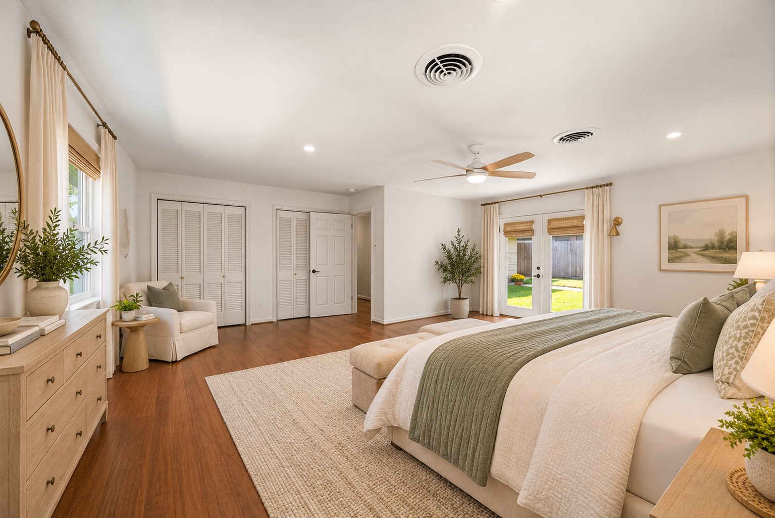 Spacious and bright bedroom with elegant wood flooring, featuring large windows and French doors that open to a lush backyard. Cozy seating area and ample closet space enhance functionality. Virtually staged