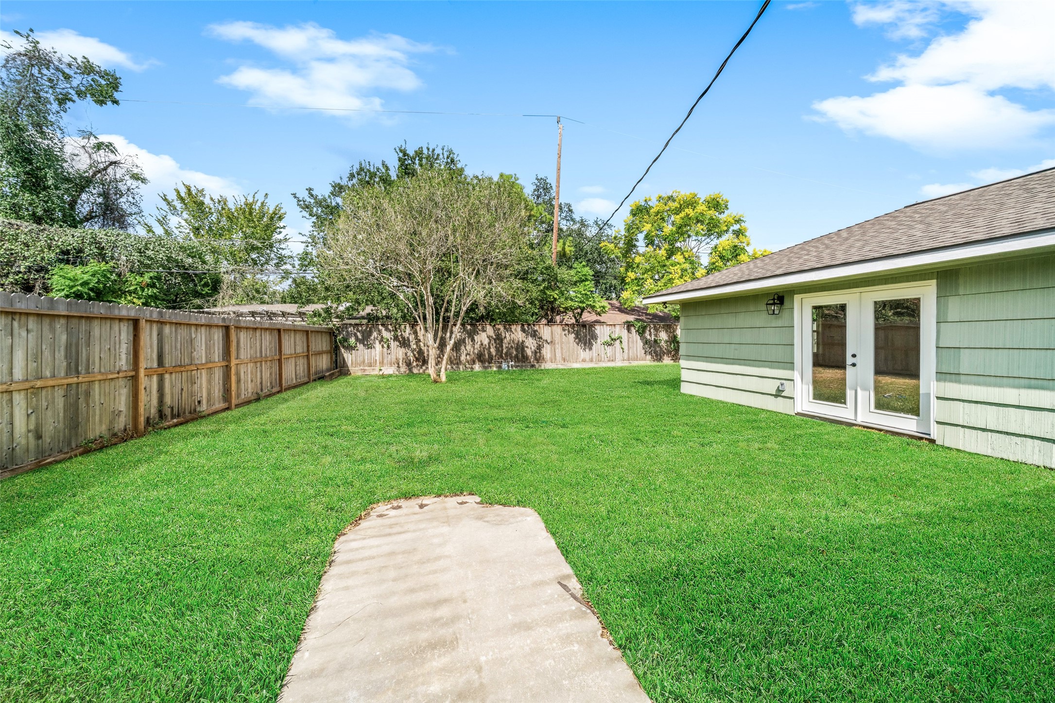 Spacious backyard with lush green lawn, a charming tree, and a private wooden fence, complemented by inviting French doors leading to the home.