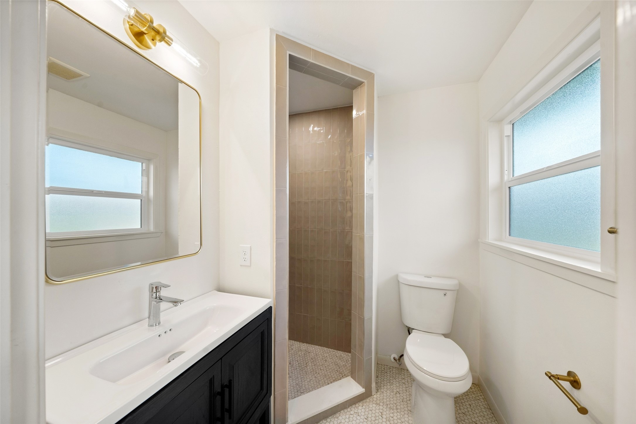 Bright and modern bathroom featuring a sleek walk-in shower, stylish vanity with a large mirror, and natural light from frosted windows.