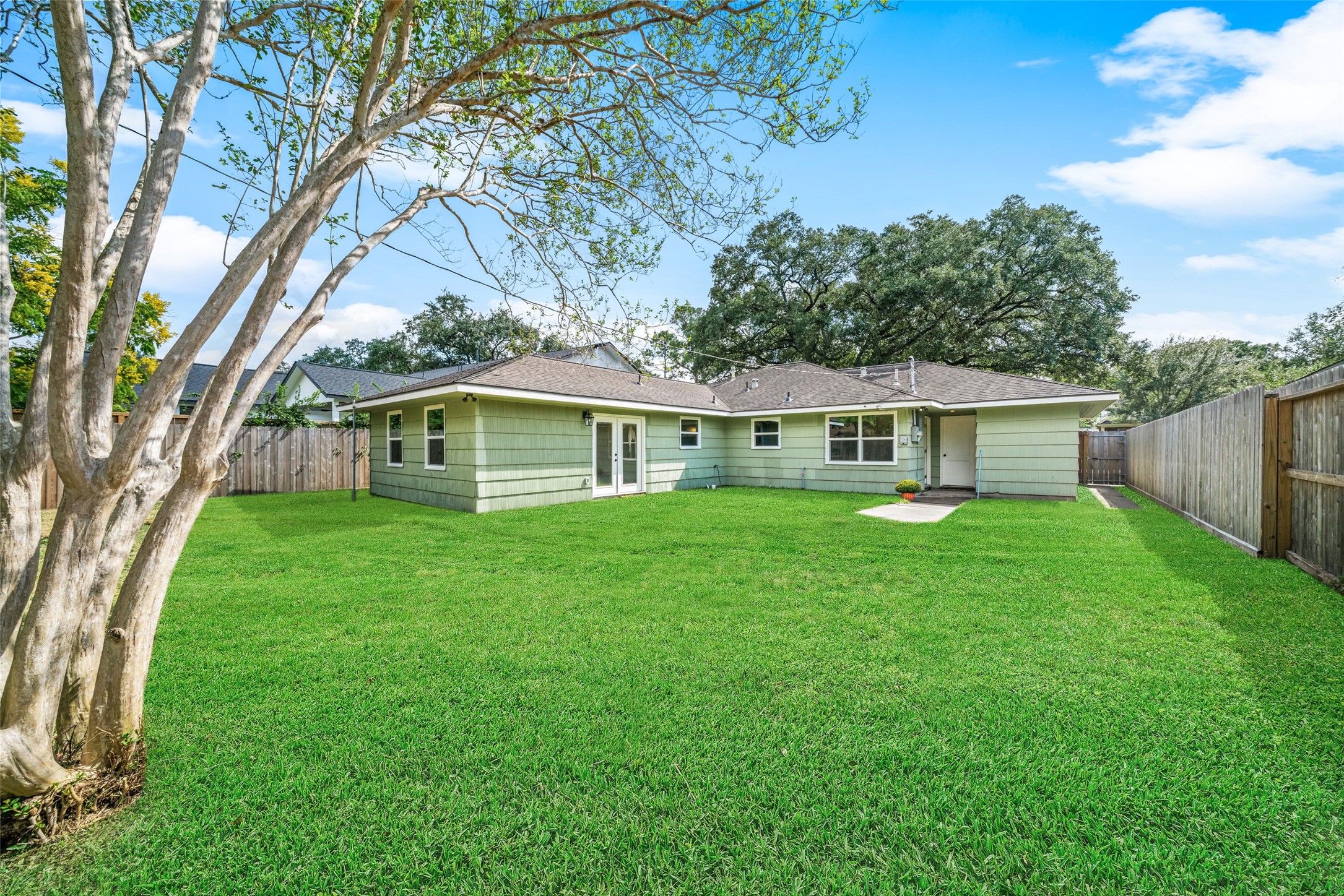 Spacious backyard with lush green lawn, mature trees, and a charming single-story home offering ample outdoor space for relaxation and entertaining.