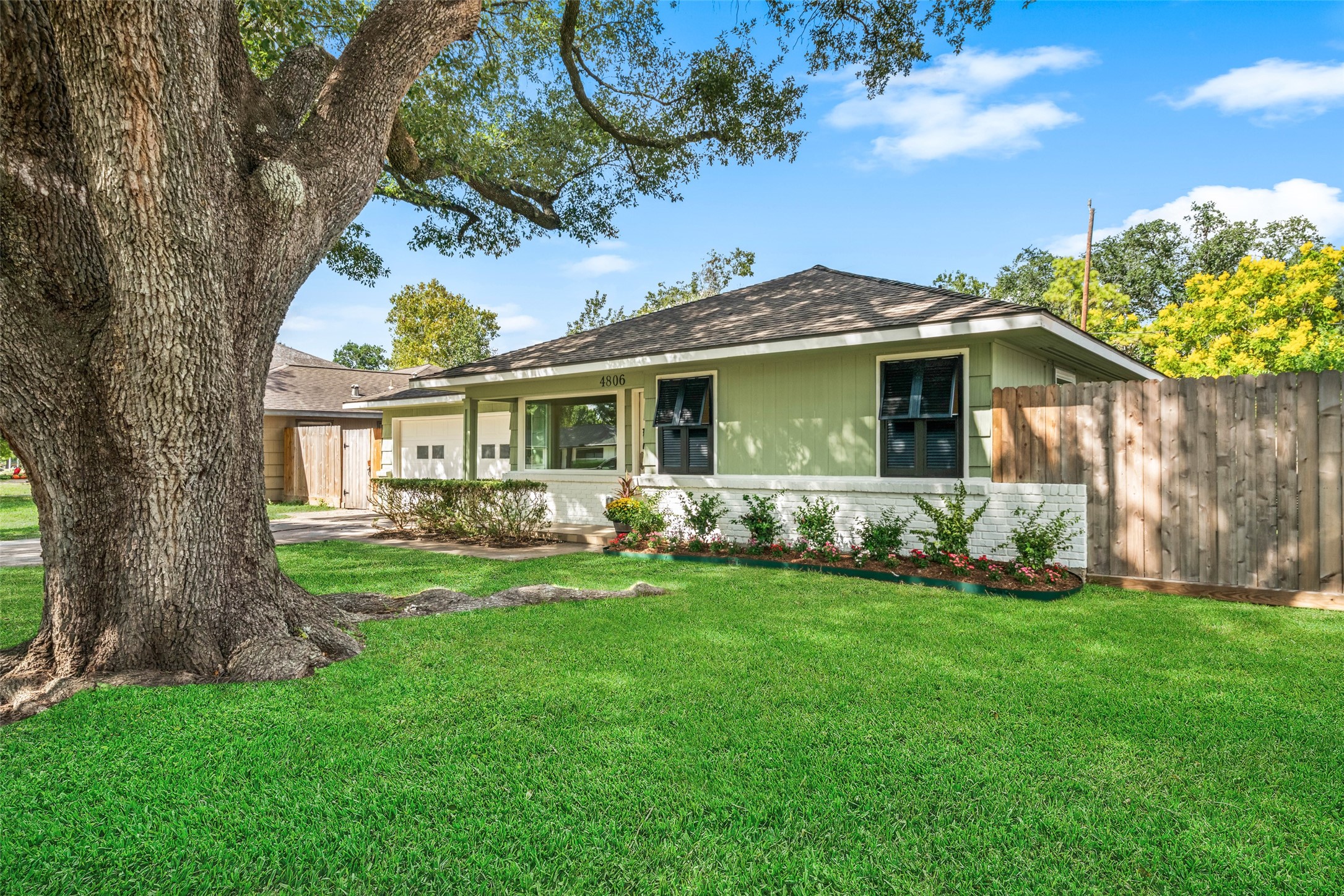Charming home with lush green lawn and mature shade tree, complemented by a welcoming front porch and privacy fence.