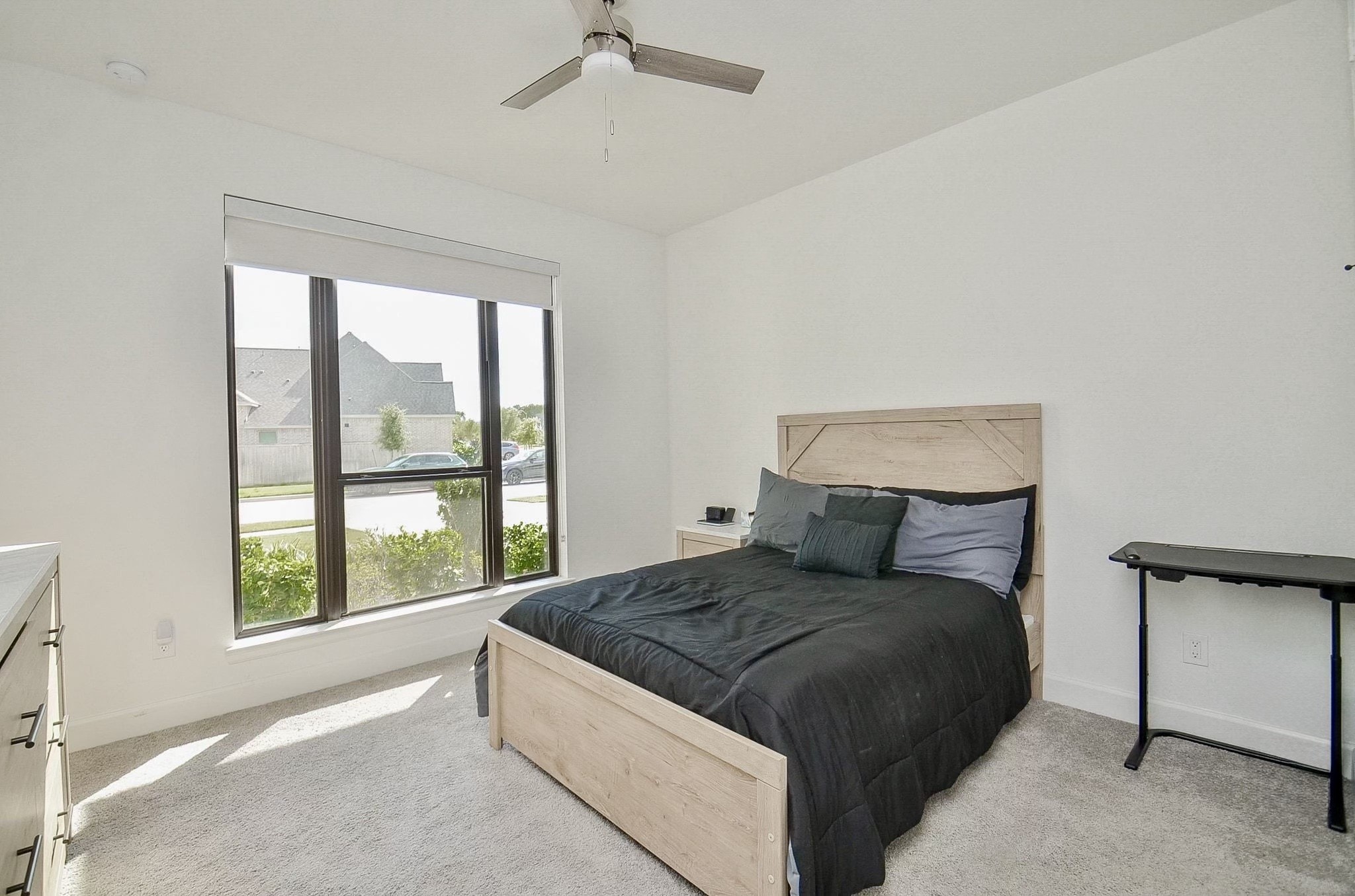 Bright secondary bedroom downstairs with large windows for natural light, and ceiling fan.