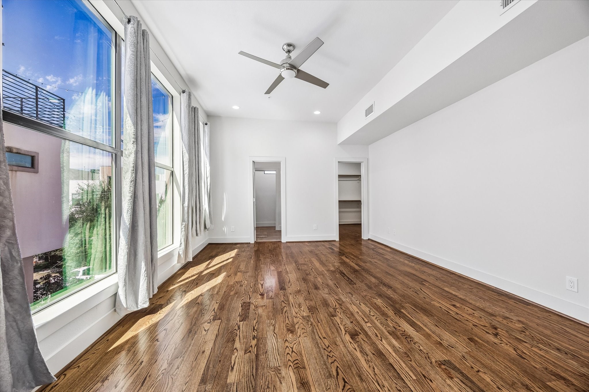 Alternate view of the primary bedroom highlighting expansive windows, a walk-in closet with built-in shelving and hanging space, and access to the adjoining bathroom.