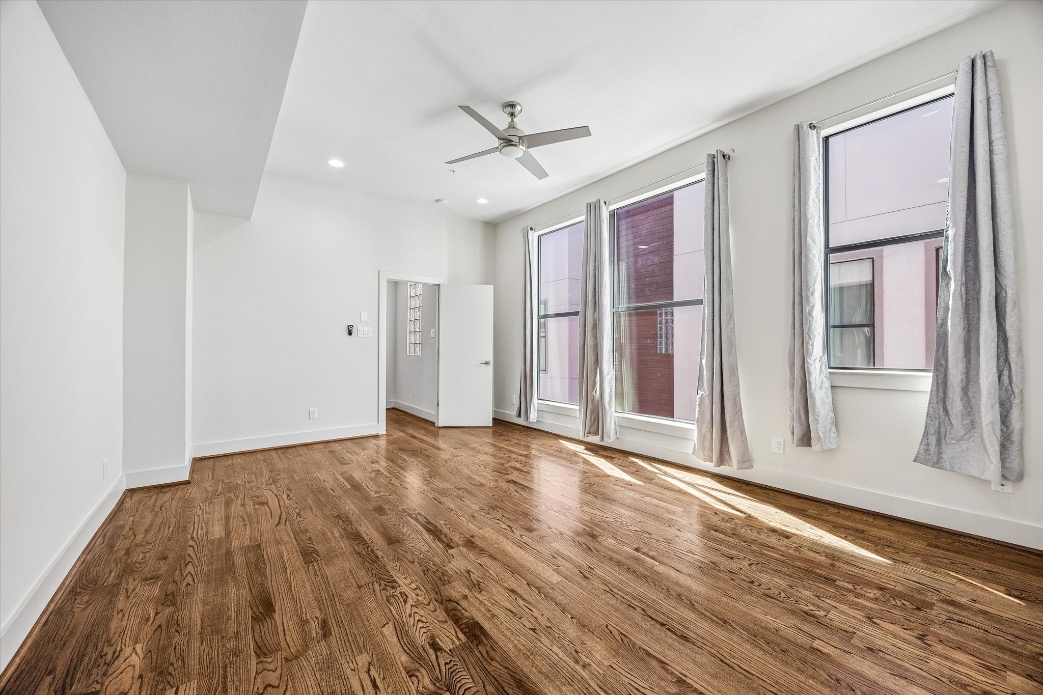 Light-filled primary bedroom with tall windows, high ceilings, wood flooring, recessed lighting, and a ceiling fan.