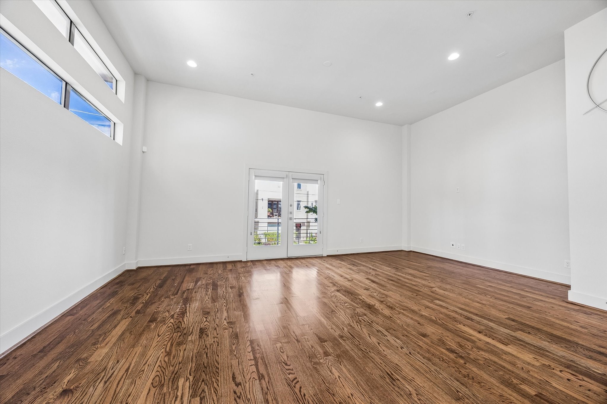 Spacious living area with high ceilings, wood flooring, recessed lighting, and large windows. French doors provide access to the balcony. Spacious living area with high ceilings, wood flooring, recessed lighting, and large windows. French doors provide access to the balcony.