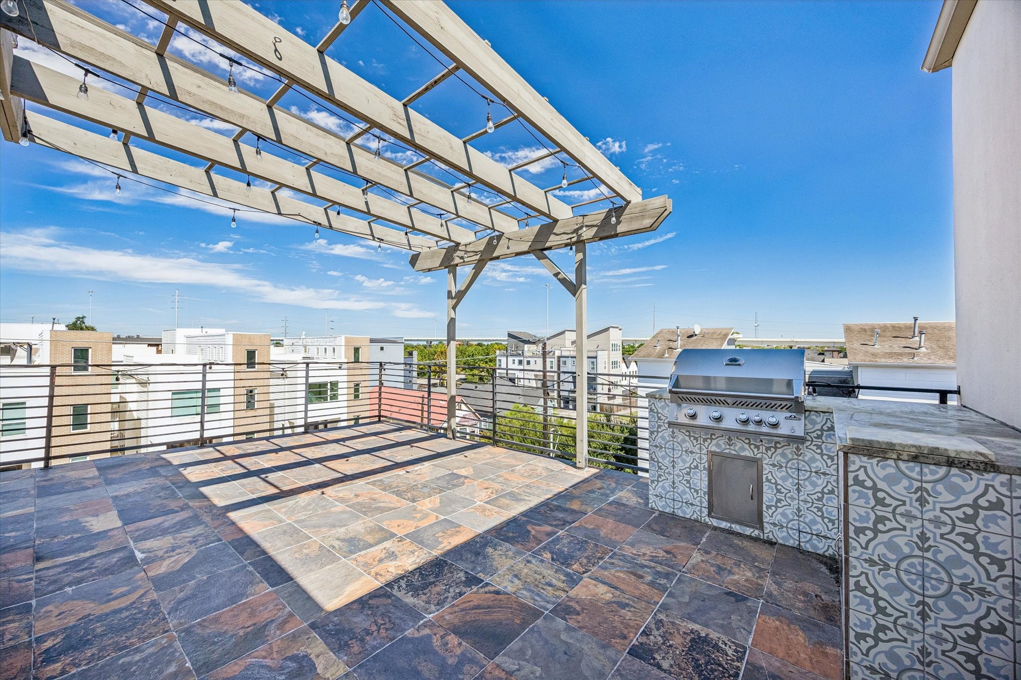 Spacious rooftop terrace featuring tile flooring, a pergola, horizontal metal railings, and a built-in grilling station with adjacent counter space.