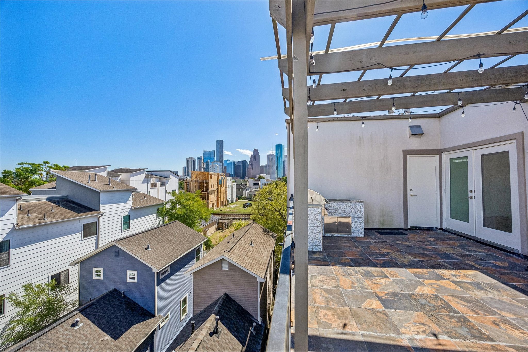 City skyline views create a striking backdrop for the rooftop terrace, featuring tile flooring, a pergola, and direct access to the upper-level interior.