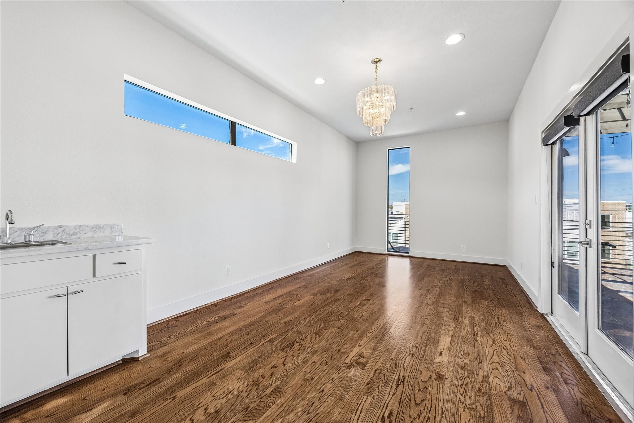 Upper-level flex space with wood flooring, clerestory windows, and a built-in wet bar. French doors connect the room directly to the rooftop terrace.