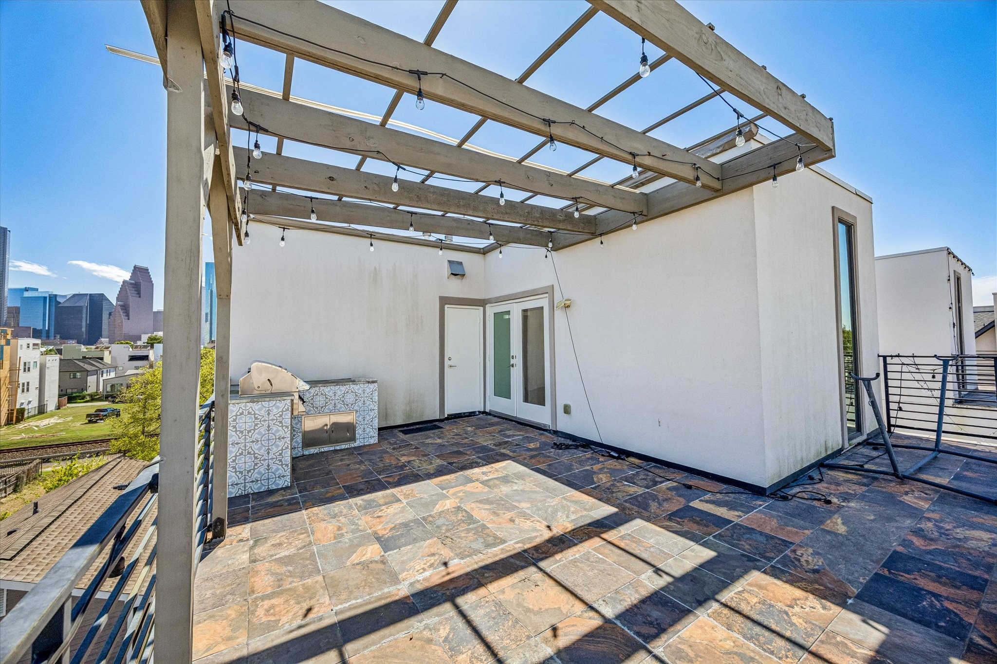 Alternate terrace view highlighting the pergola, built-in grilling station, and French doors connecting to the interior. The open layout provides room for outdoor entertaining with skyline views.