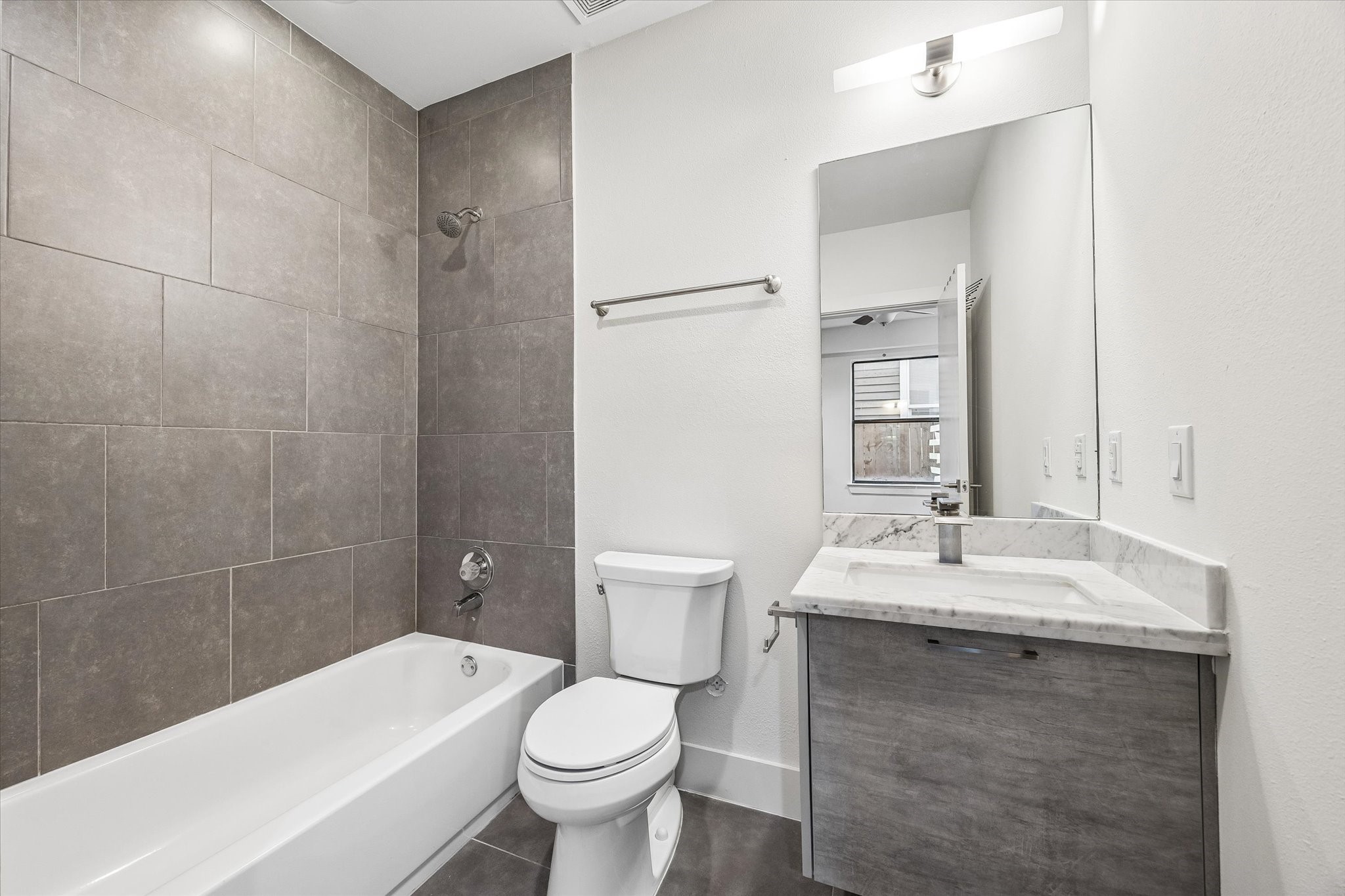 Full bathroom with a tub/shower combination, full-height tile surround, tile flooring, and a vanity with an undermount sink and cabinet storage.