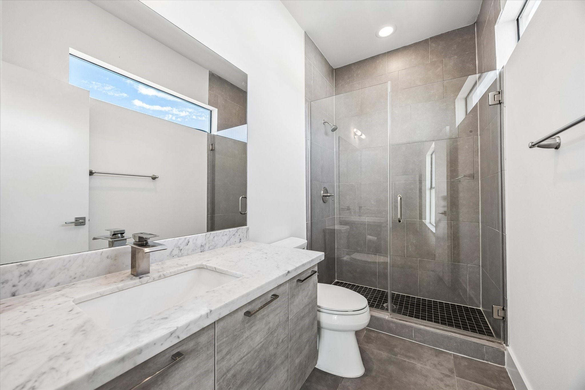 Full bathroom featuring a glass-enclosed walk-in shower, full-height tile, and a clerestory window. A spacious vanity provides counter space and storage.