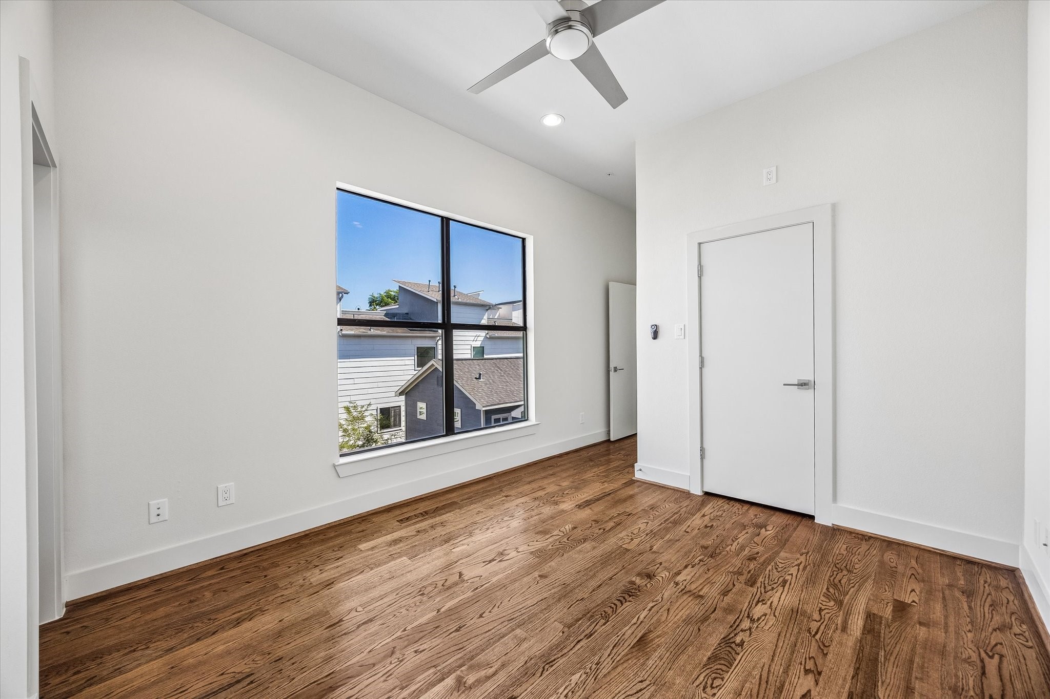 Secondary bedroom located on the third floor. Bright bedroom featuring an oversized window, wood flooring, high ceilings, recessed lighting, and a ceiling fan.