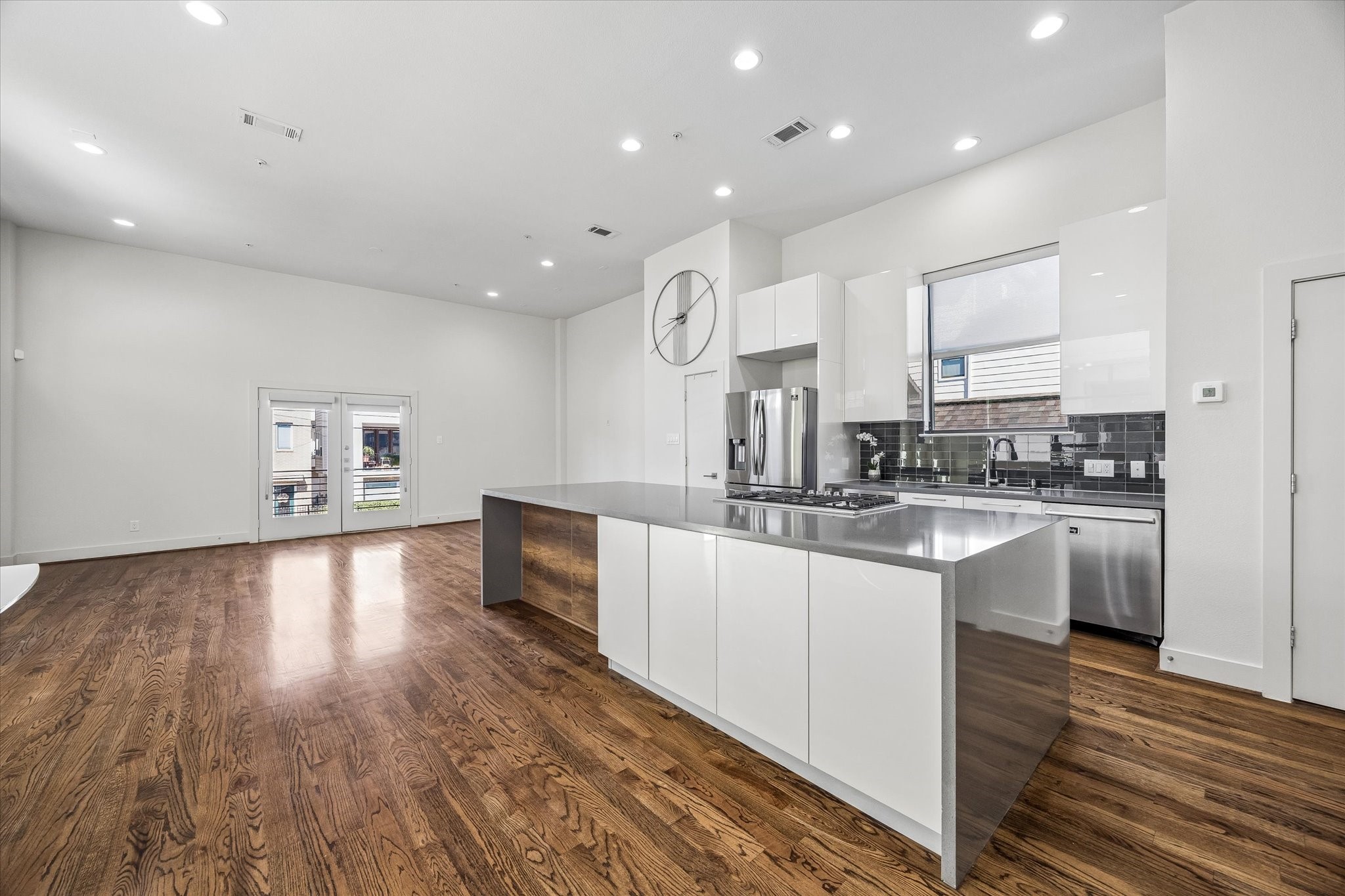 Kitchen overlooking the living area, featuring a large island with a gas cooktop, sleek white cabinetry, stainless steel appliances, and a contrasting tile backsplash.