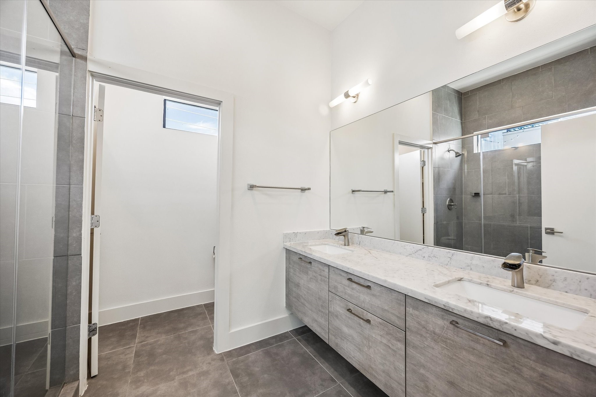 Primary bathroom featuring a spacious double-sink vanity, a broad mirror, tile flooring, and a glass-enclosed shower with full-height tile.