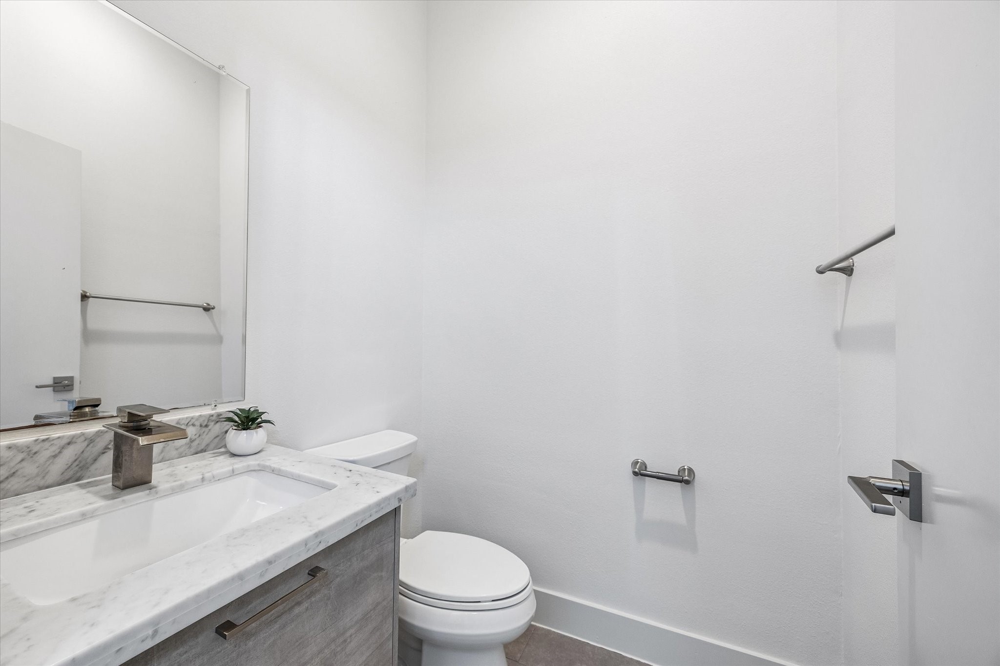 Convenient powder room featuring a vanity with a veined countertop, an undermount sink, cabinet storage, and a large mirror.