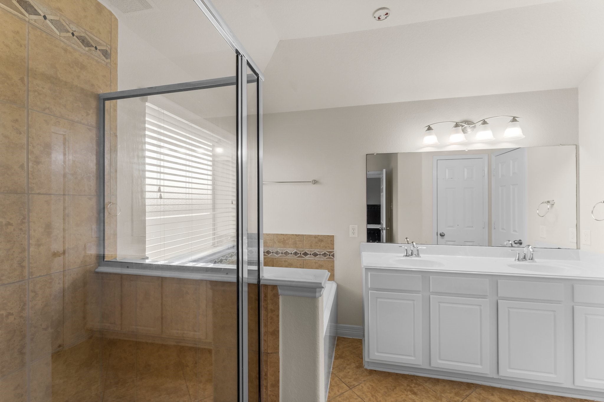 Spacious bathroom featuring a glass-enclosed shower, double vanity with sleek fixtures.