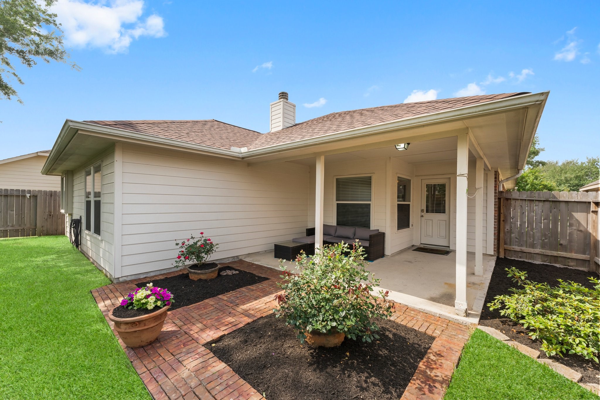 Enjoy the covered patio, lush green lawn, and tasteful landscaping with flower beds and potted plants.
