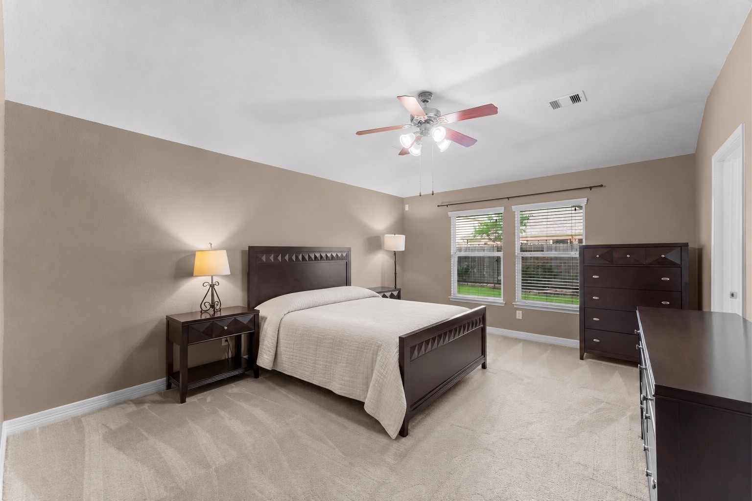 Primary bedroom with abundant natural light from two large windows overlooking the backyard.