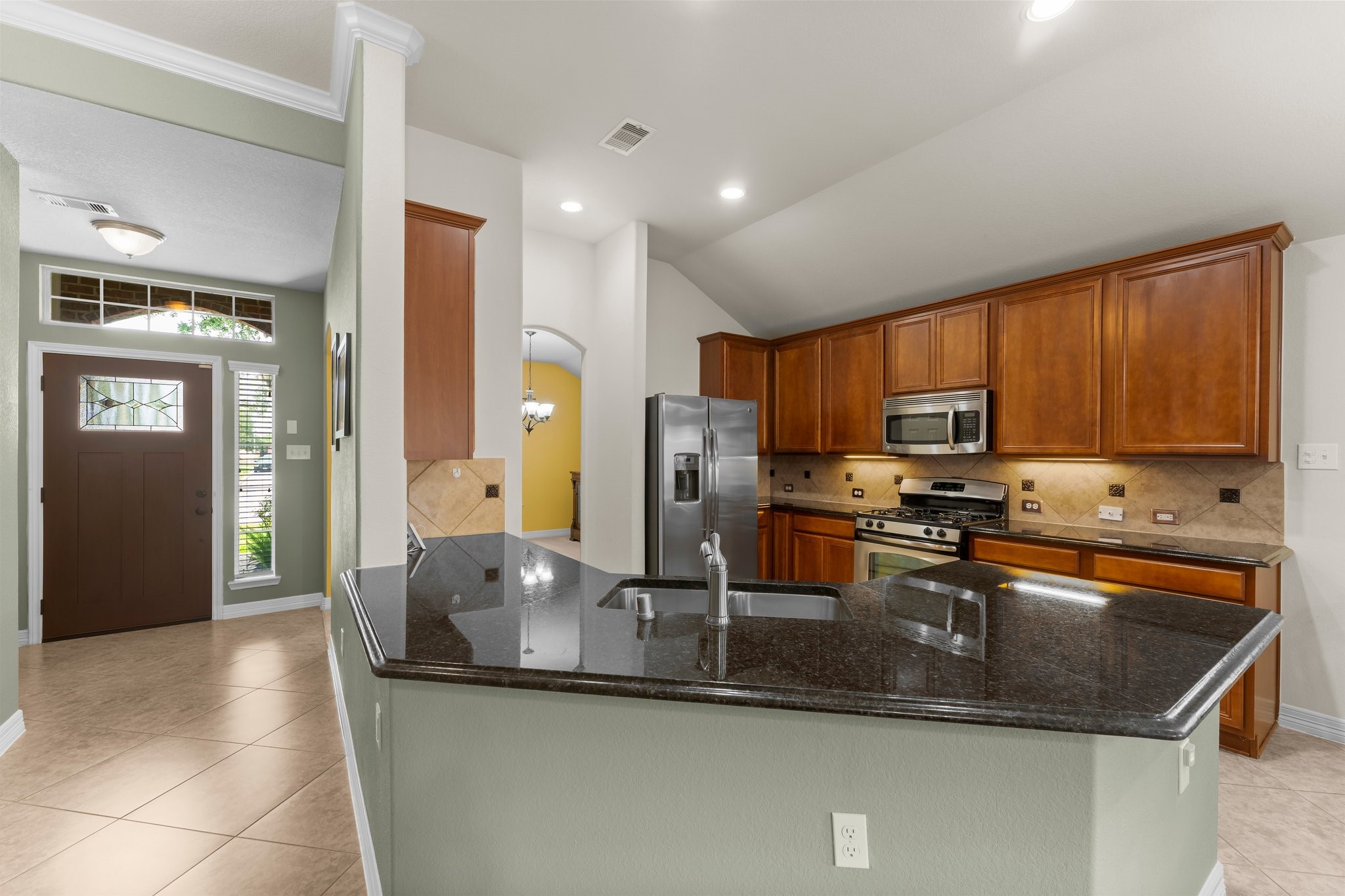Elegant kitchen with granite countertops, stainless steel appliances, and rich wood cabinetry, seamlessly flowing into a welcoming entryway.