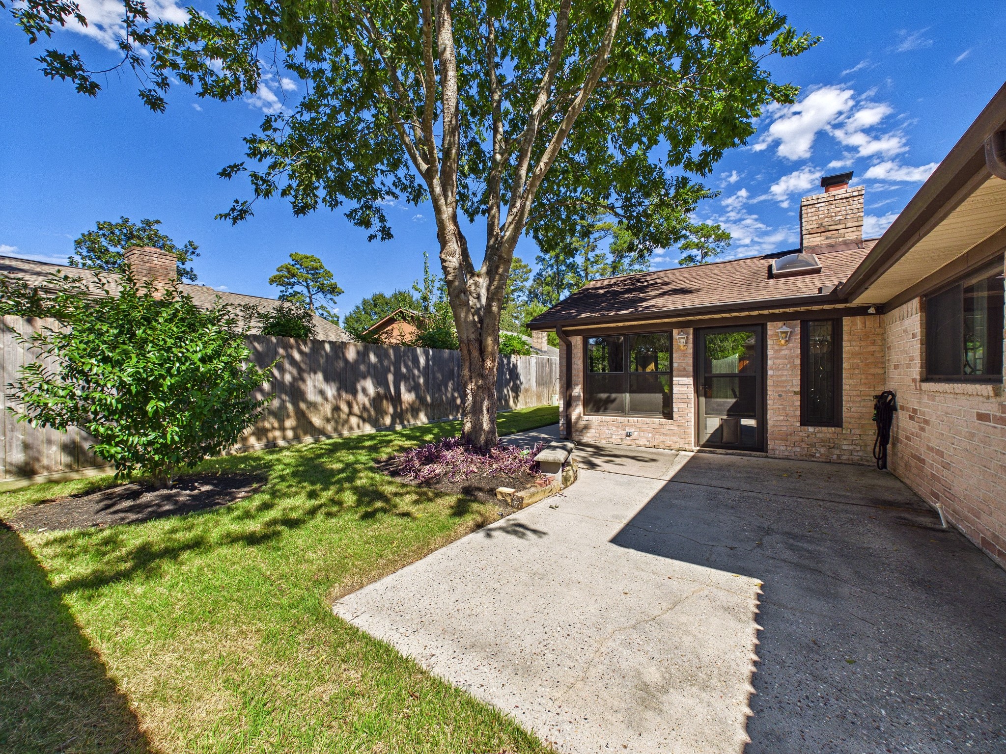 Charming backyard with a spacious patio, lush greenery, and a mature tree offering shade and privacy, perfect for outdoor relaxation and gatherings.