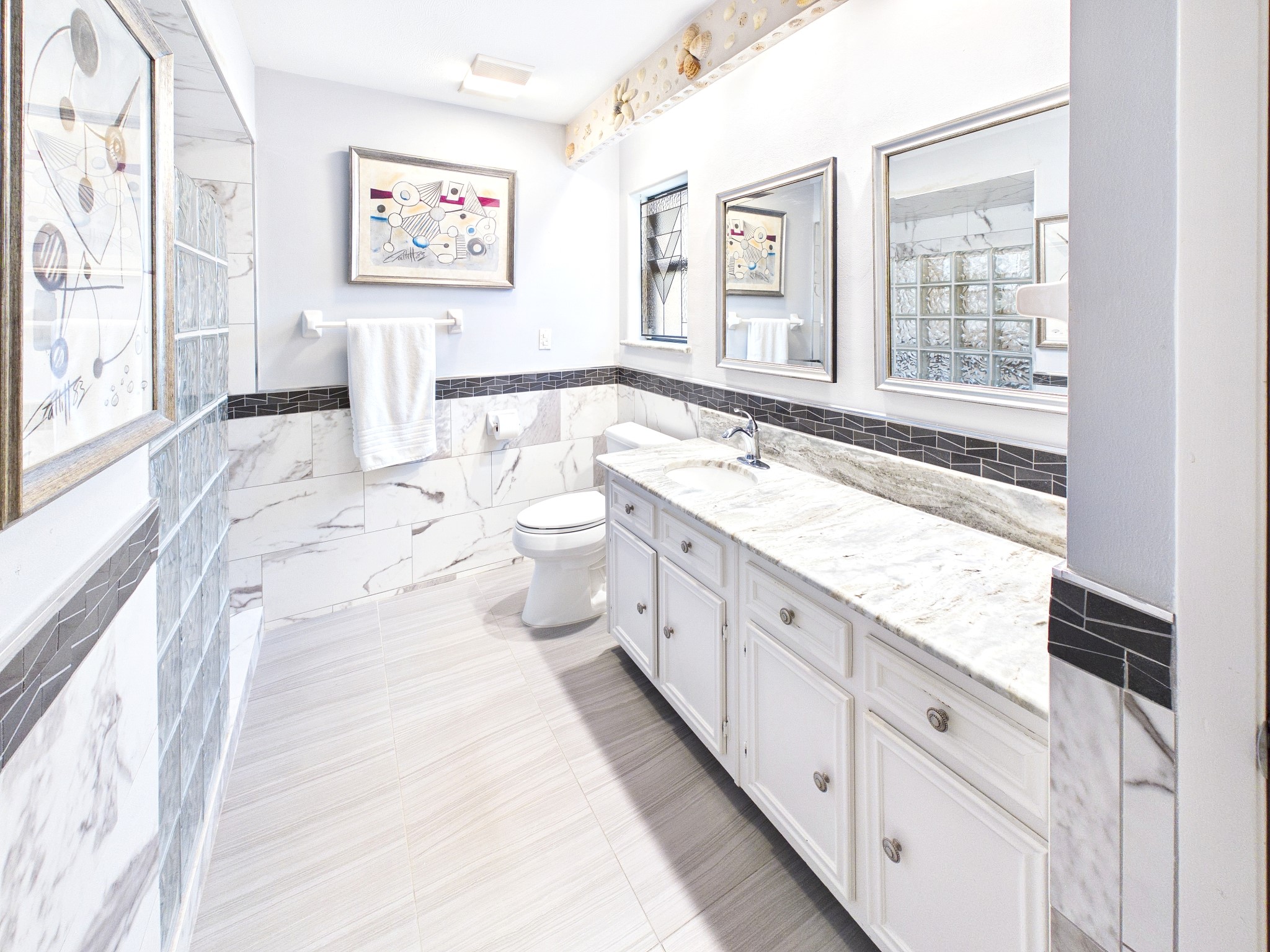 Luxuriate in the serene elegance of this primary bath, featuring a stunning marble-topped double vanity, chic modern tiles, and abundant natural light that elevates your daily routine.