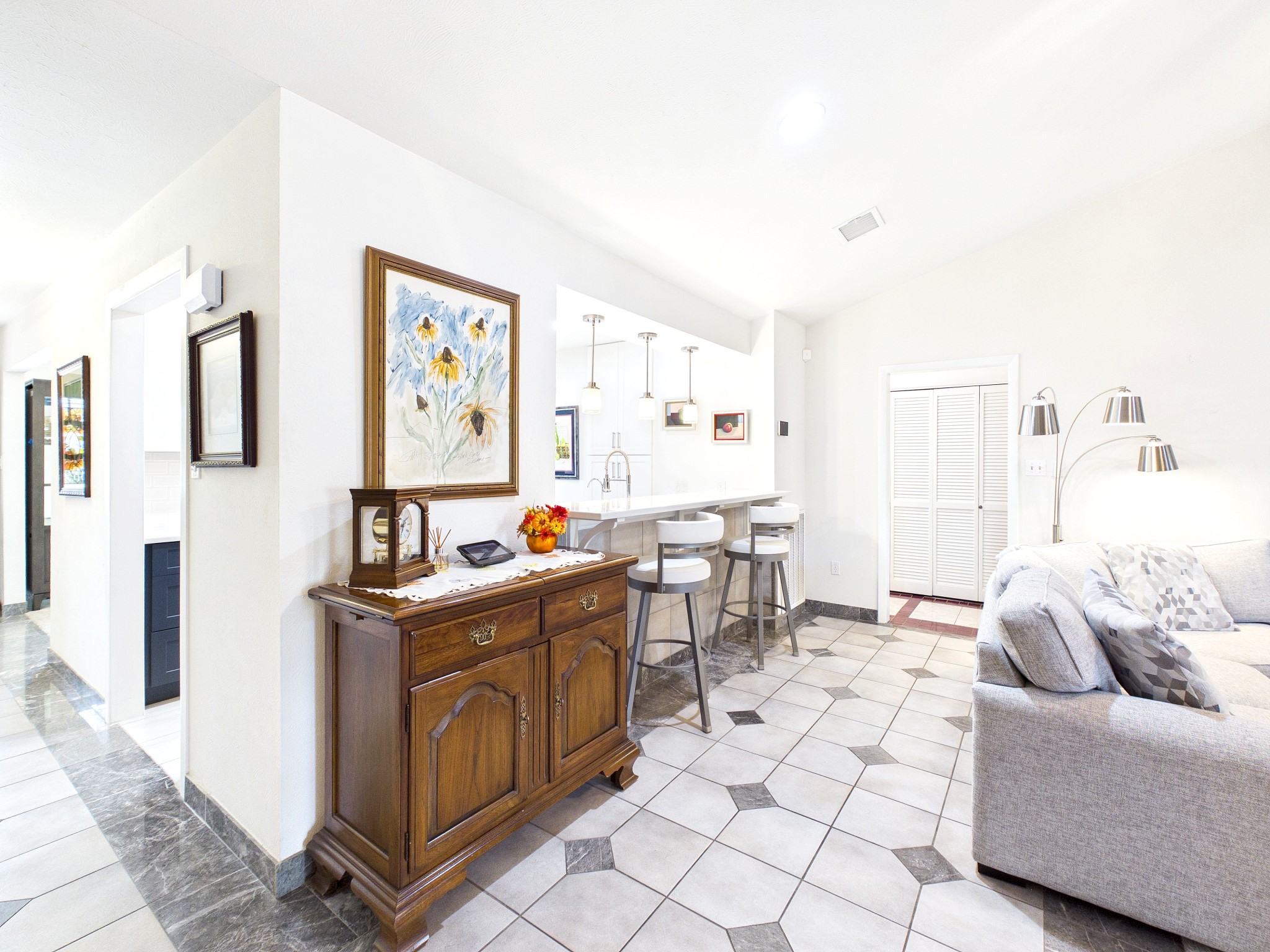 Charming open-concept living area with a cozy sofa and stylish breakfast bar, featuring modern pendant lighting and elegant tile flooring.