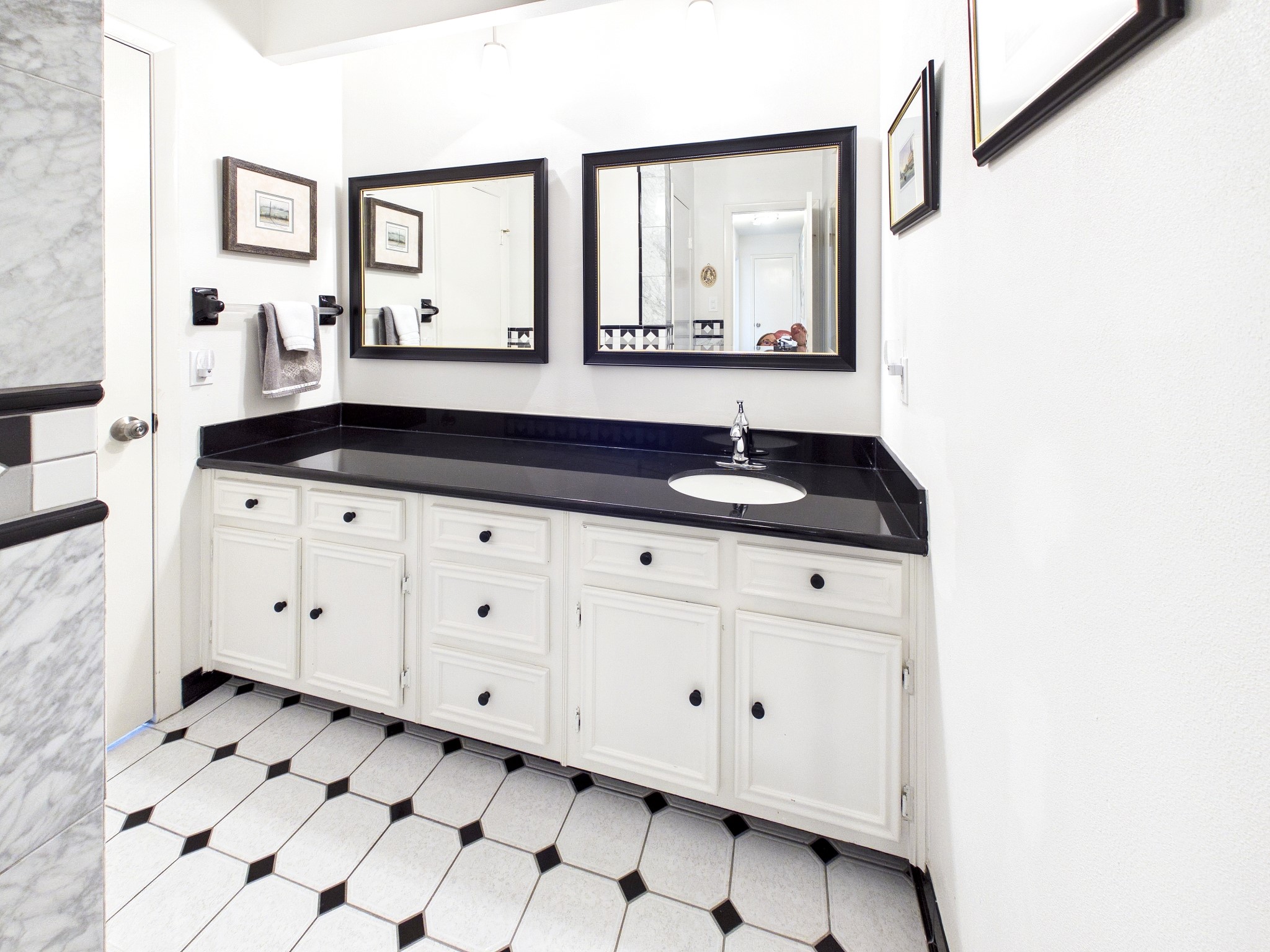 Elegant black and white tiles set the stage for a sophisticated bathroom featuring sleek countertops and ample cabinet space.