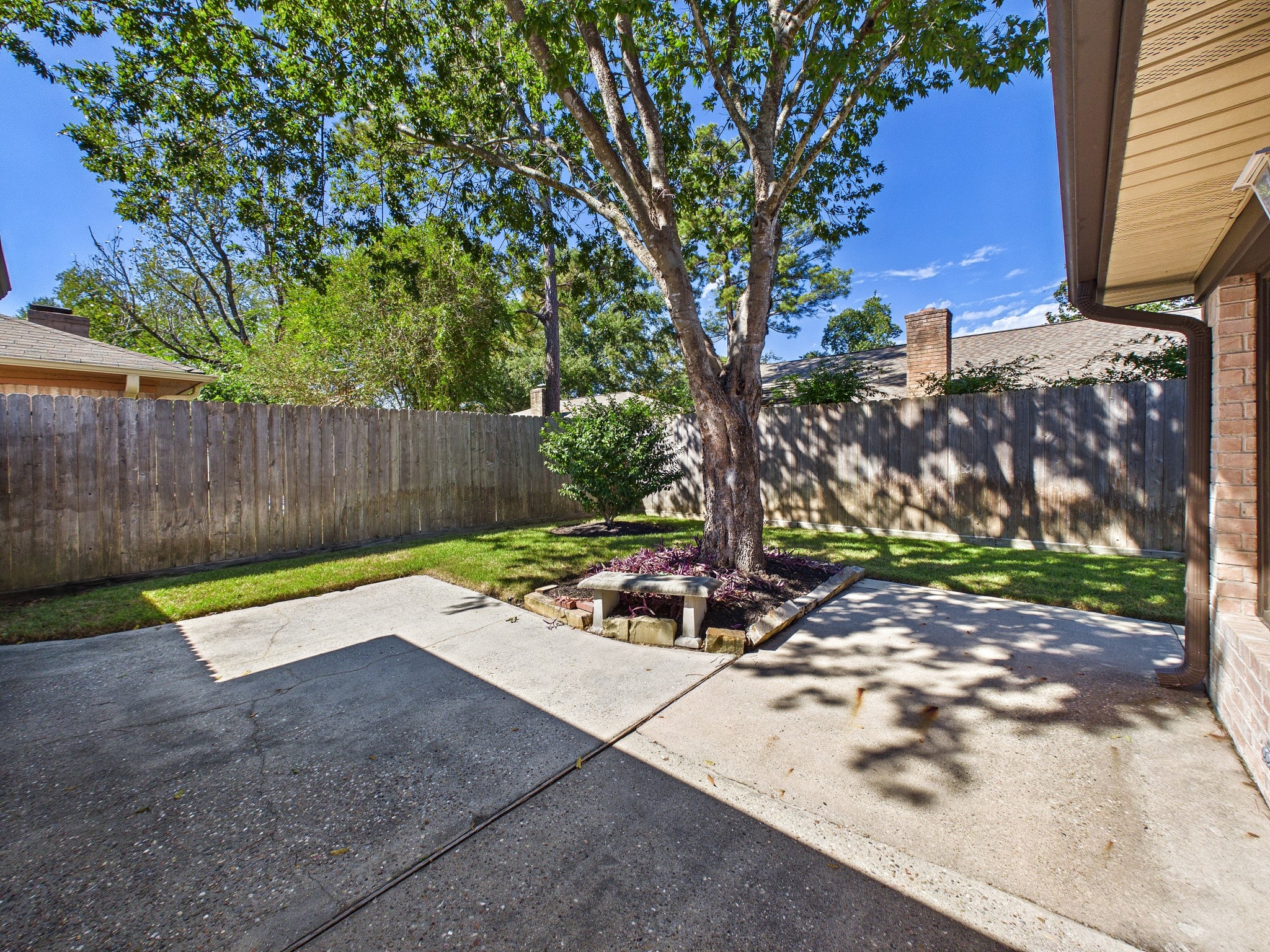Charming backyard oasis with a spacious patio, lush greenery, and a mature shade tree, perfect for relaxation and outdoor entertaining.