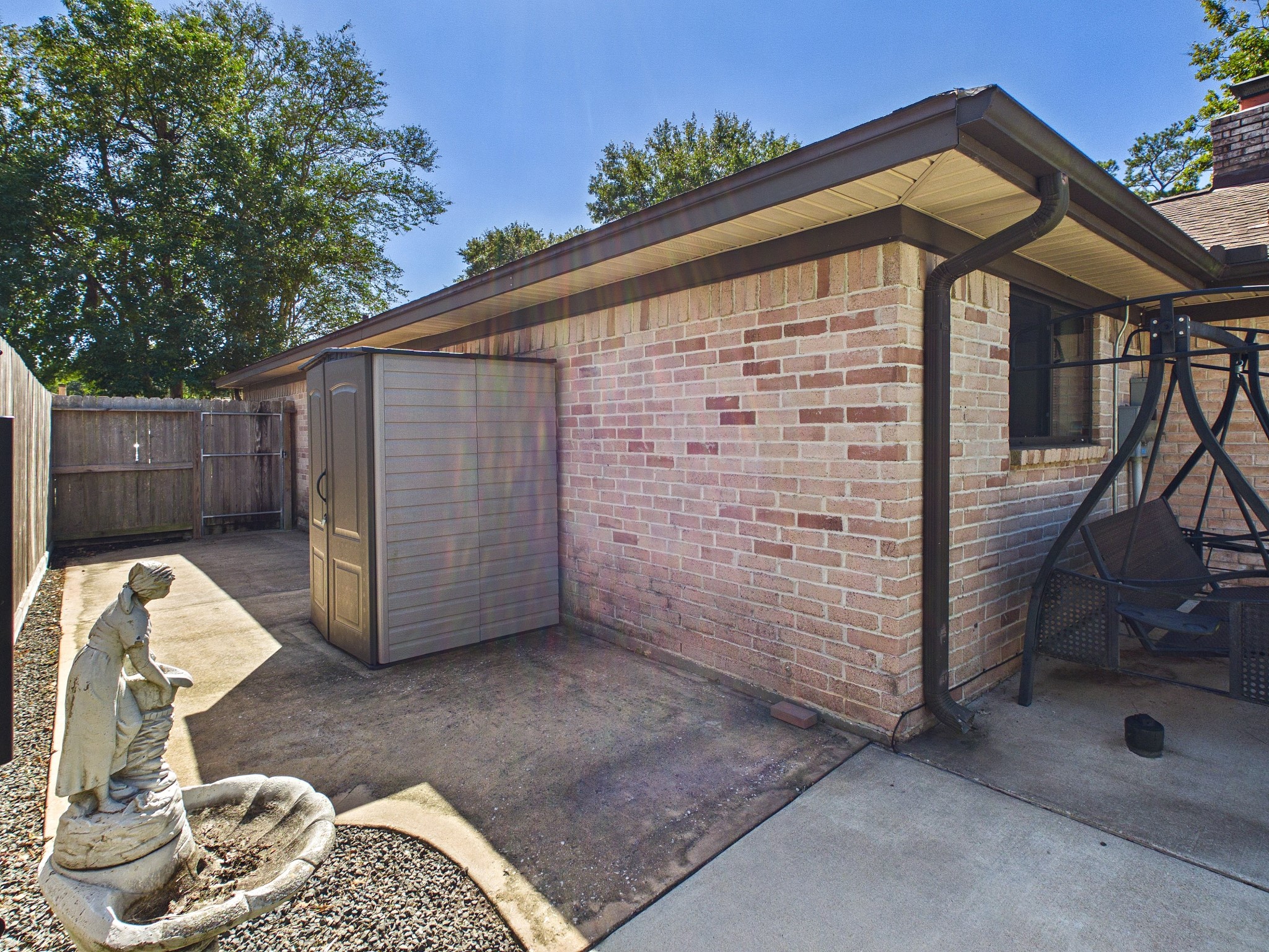 Charming backyard space with a paved patio, featuring a storage shed and a decorative statue, perfect for outdoor relaxation and storage needs.
