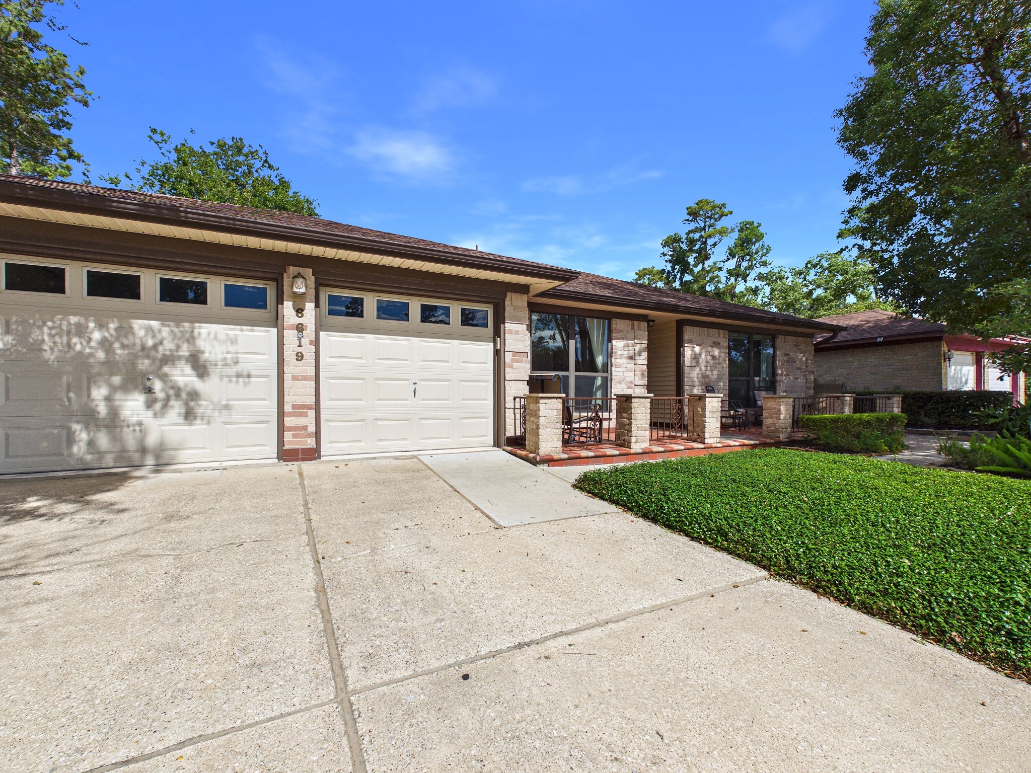 Spacious single-story home with a large two-car garage, charming brick accents, and inviting front porch, surrounded by well-maintained landscaping.