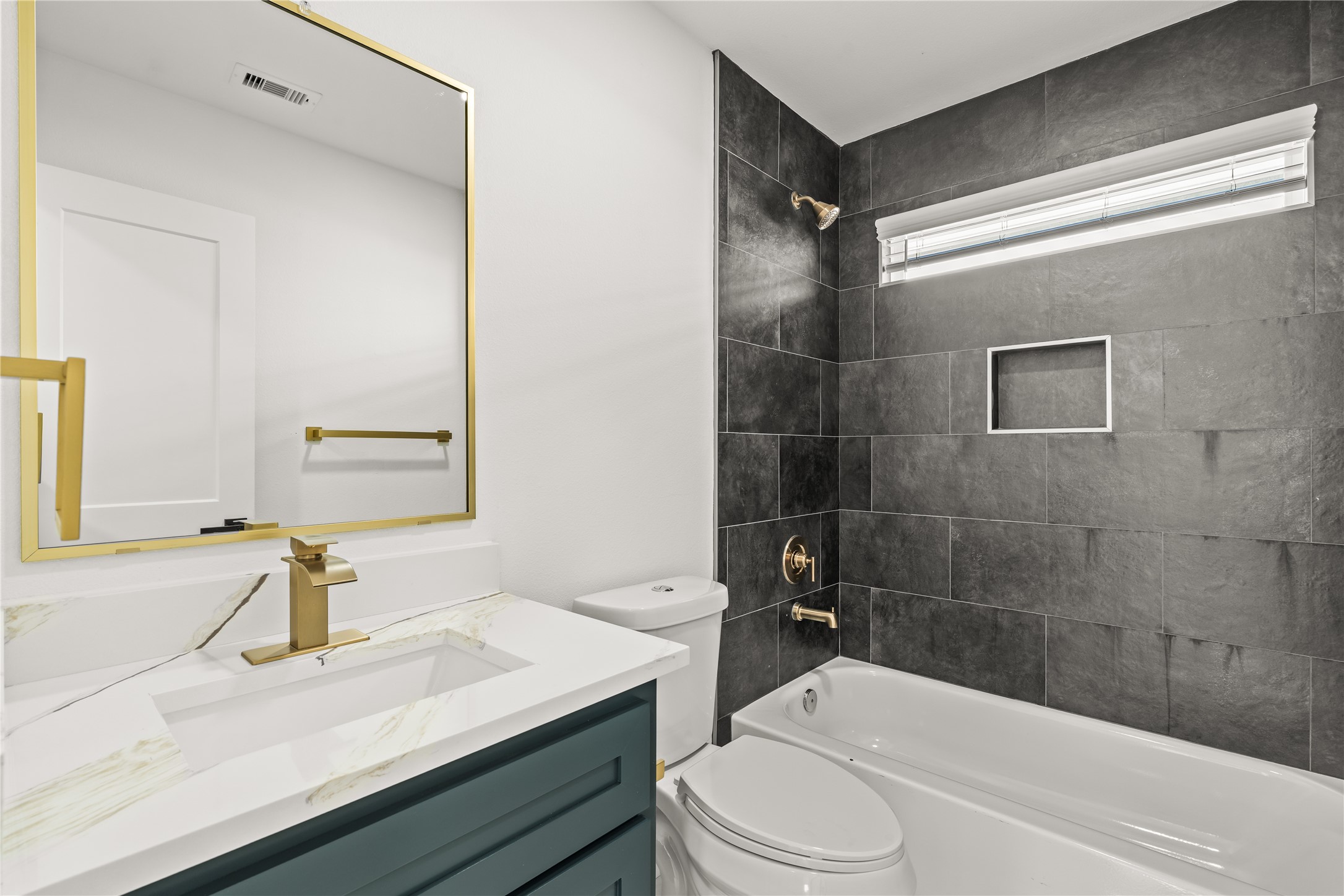 Bold, dramatic style. The full upstairs guest bathroom showcases a striking floor-to-ceiling charcoal tile accent wall paired with an elegant emerald vanity and gold hardware.
