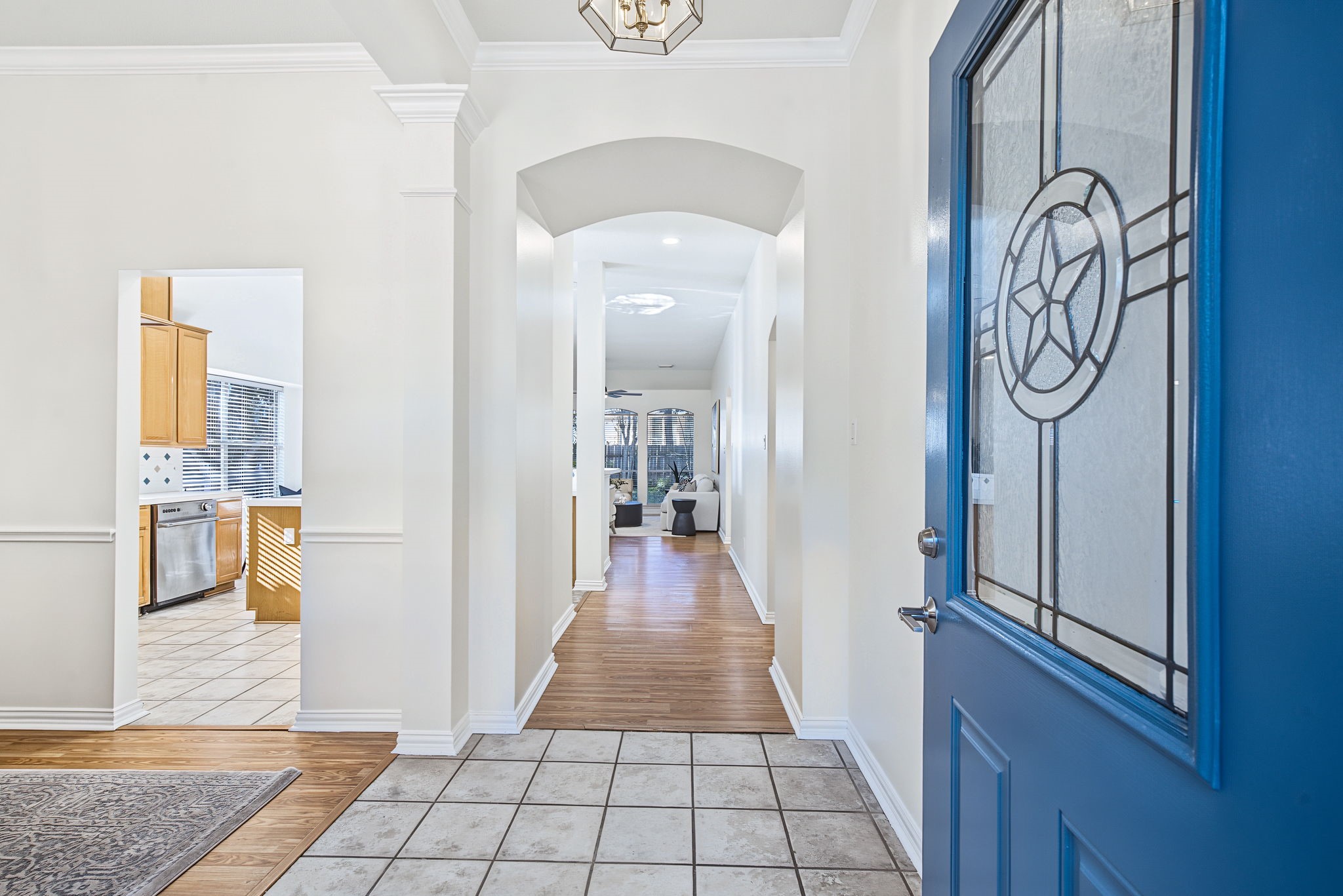 A decorative glass front door opens to a bright entry with arched architectural details, fresh neutral paint, and a welcoming view into the home.