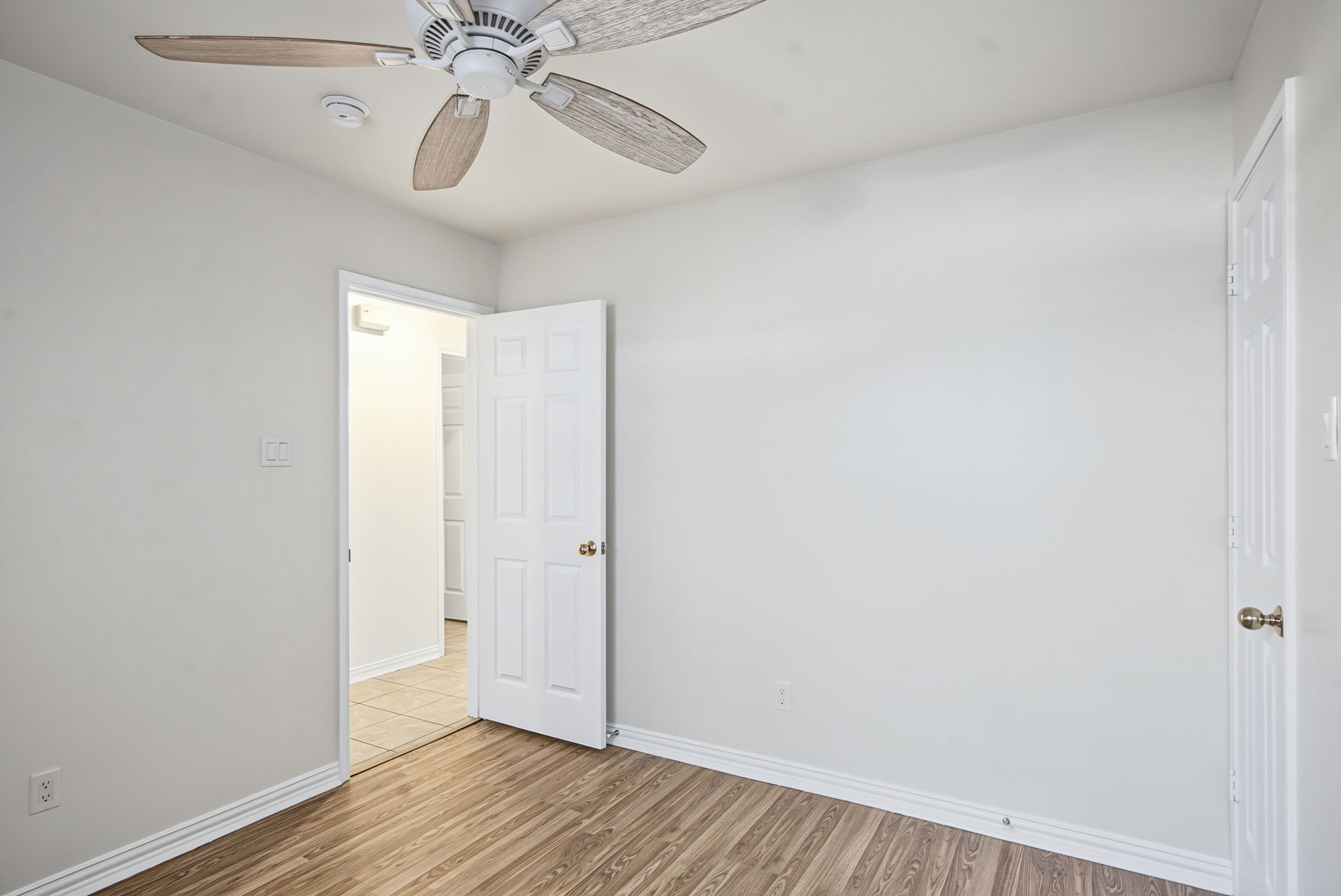 Fresh neutral paint, wood-look flooring, and a ceiling fan create a versatile secondary bedroom ready for your furnishings.