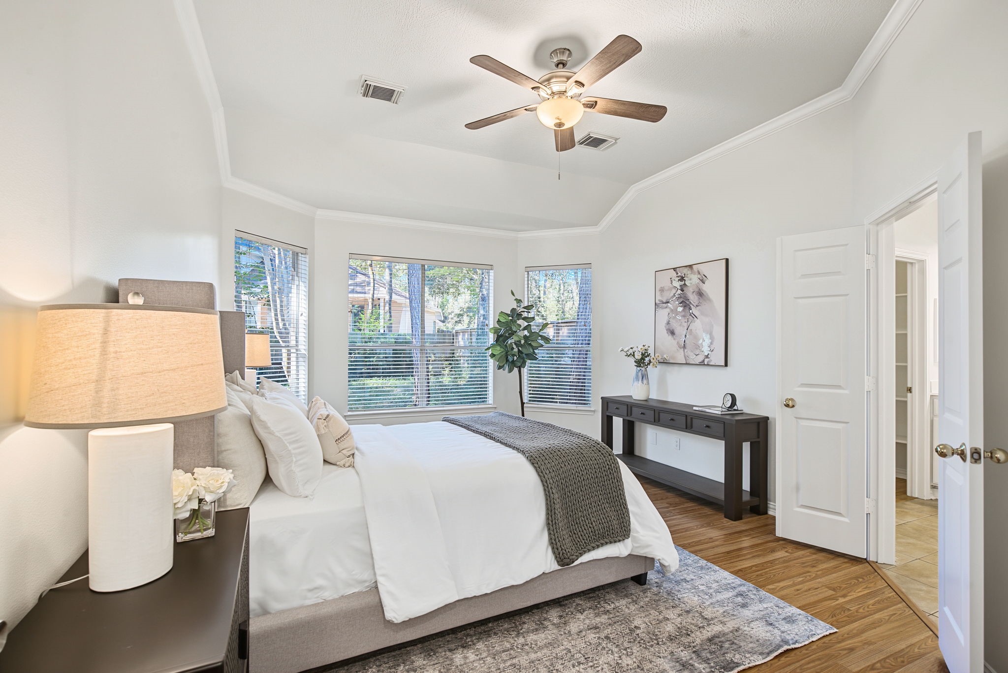The primary suite offers a retreat with a raised ceiling, crown molding, and a window-lined wall overlooking the backyard.