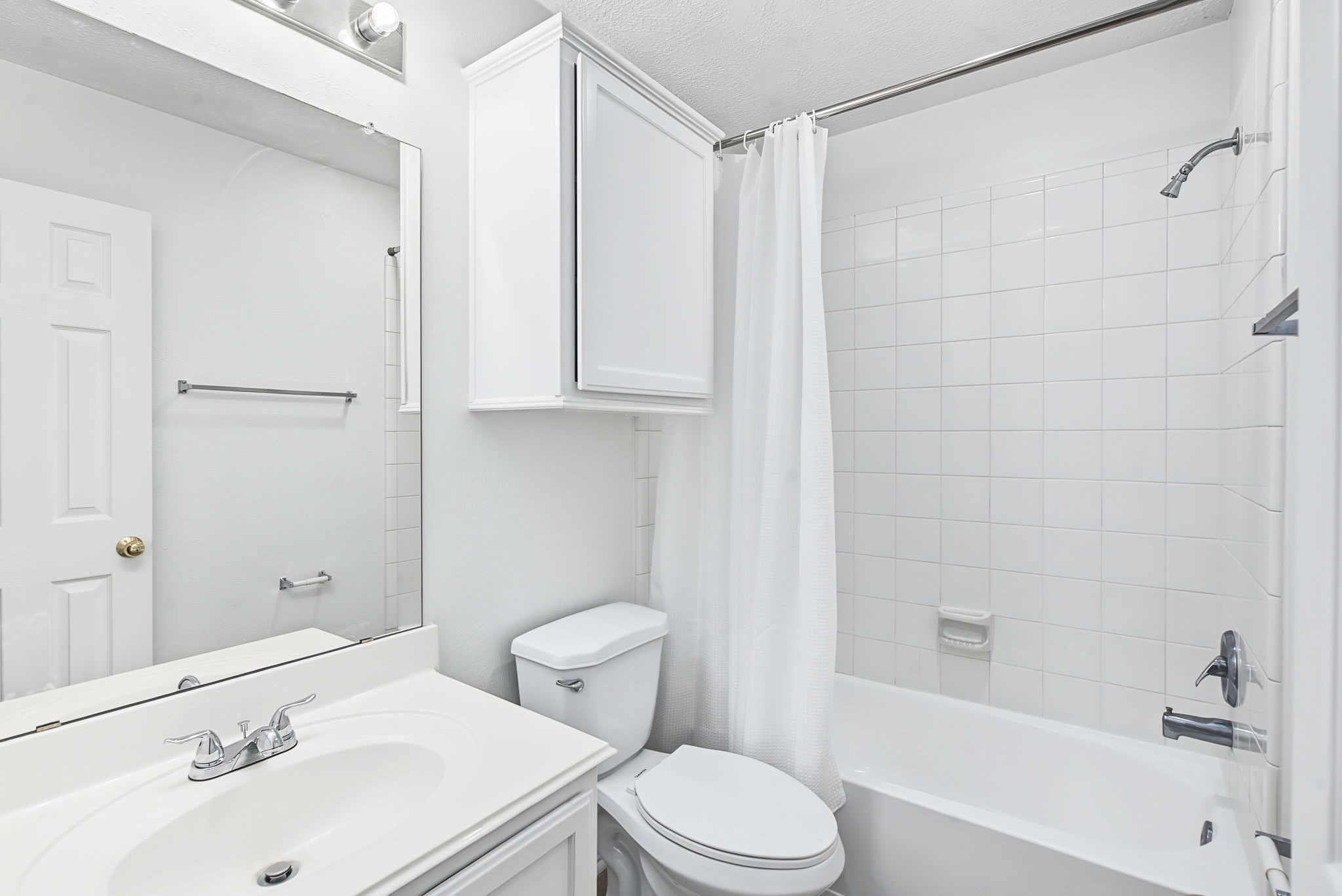 The refreshed guest bathroom features a white vanity, additional wall storage, and a tub-and-shower combination.
