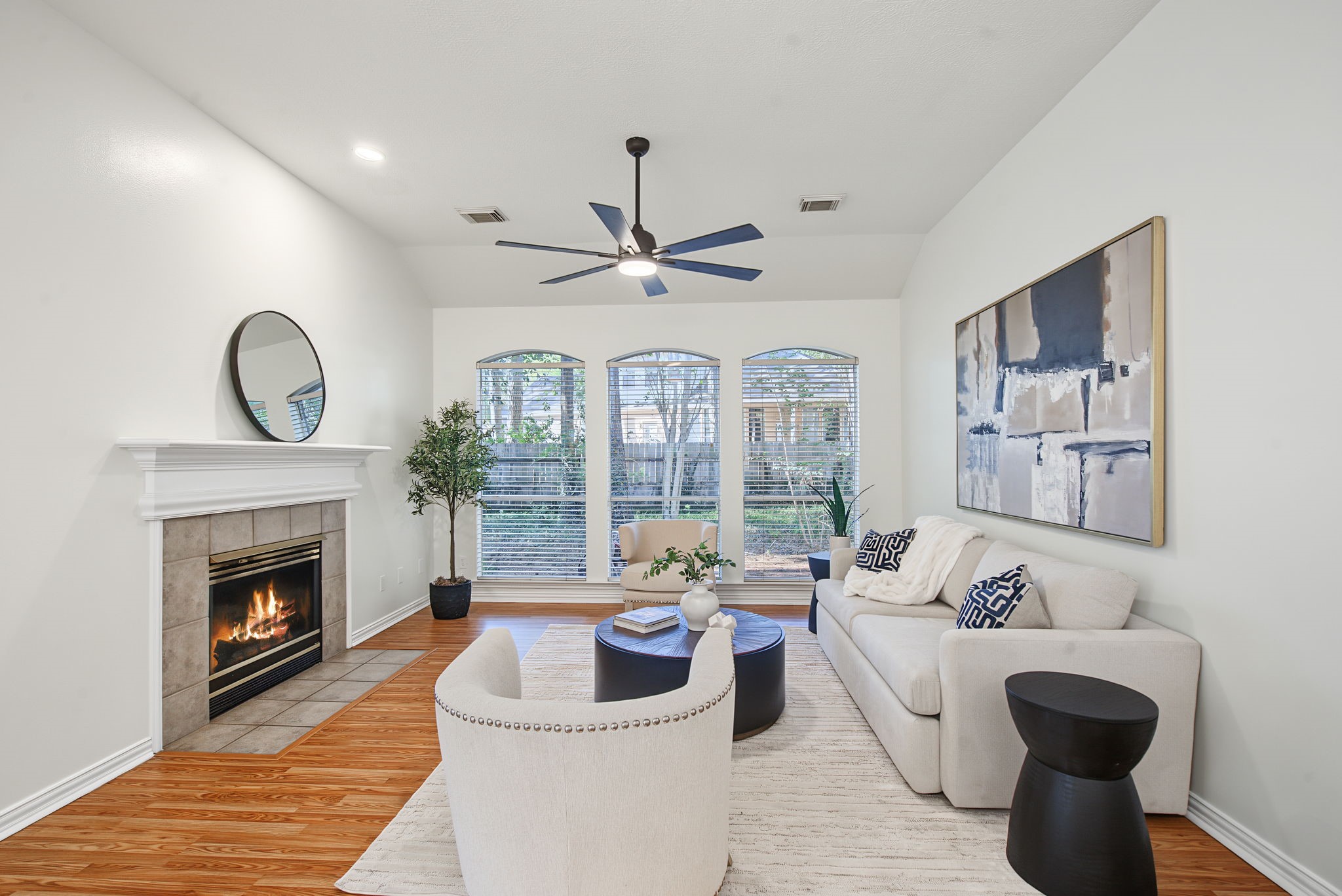 Gather around the fireplace in a living room filled with natural light, backyard views, and warm wood-look flooring.
