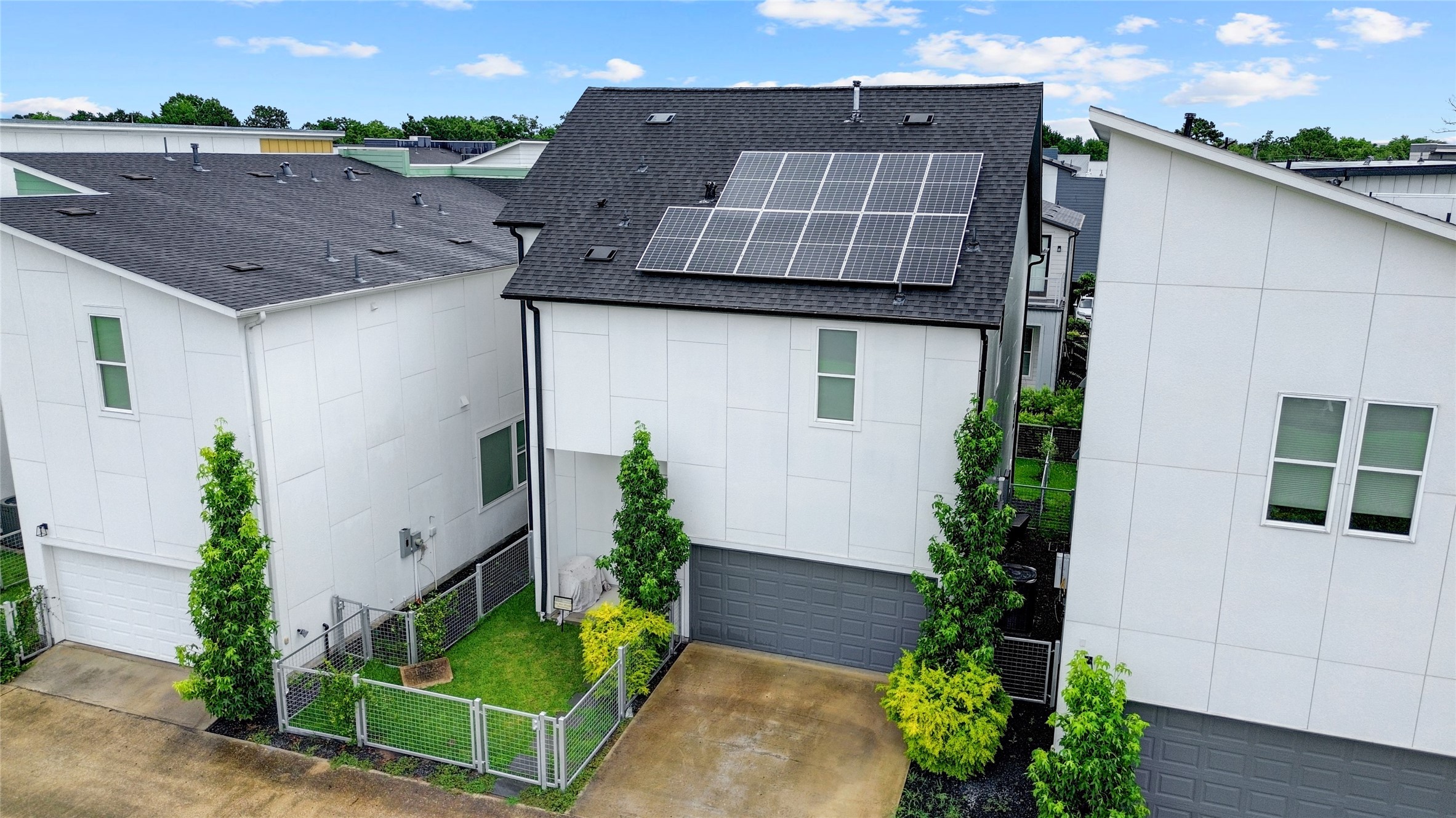 Modern home rear view, with sleek solar panels and a double wide driveway and spacious two-car garage, nestled between lush greenery and a well-maintained fenced yard.