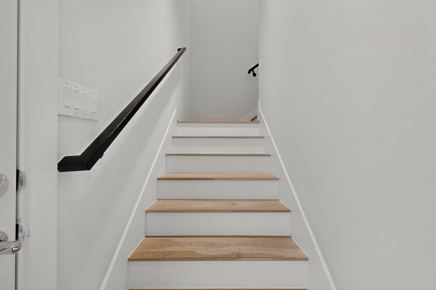 Stylish staircase featuring light wood steps and sleek black handrails, exuding modern elegance.