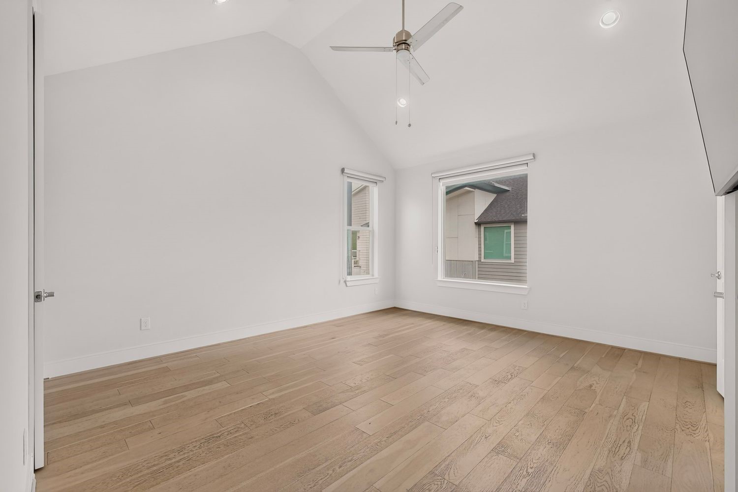 A vacant view of the bright and airy bedroom featuring vaulted ceilings, large windows for natural light, and sleek wood flooring, creating a serene and inviting space.