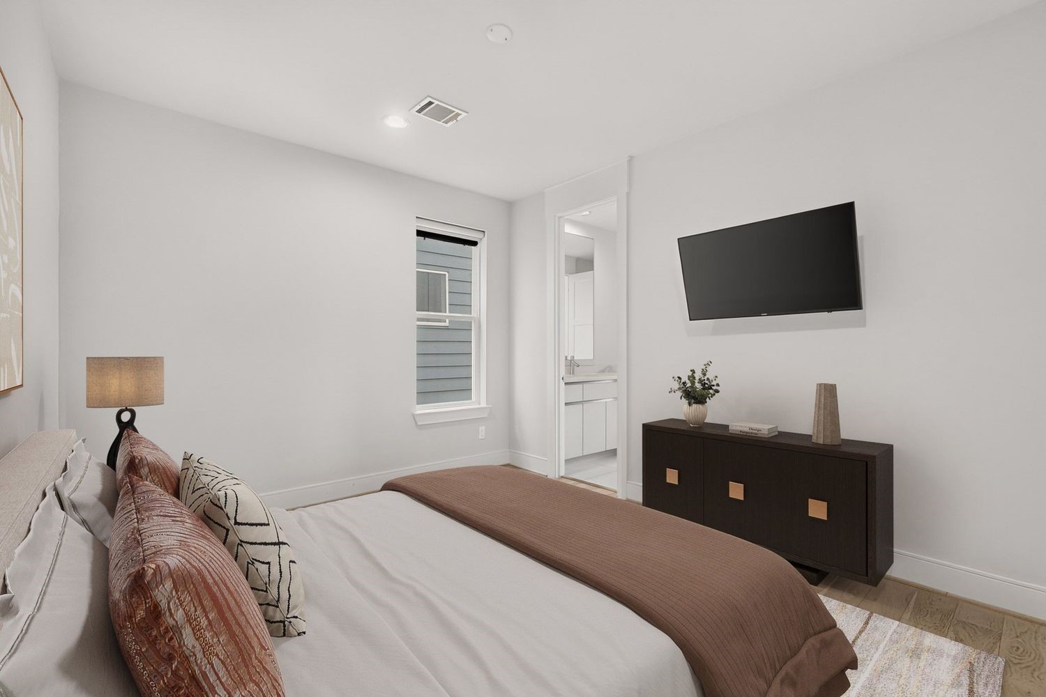 a second cozy guest bedroom with a neutral palette, featuring a comfortable bed, modern dresser, wall-mounted TV, and access to the shared en-suite bathroom.