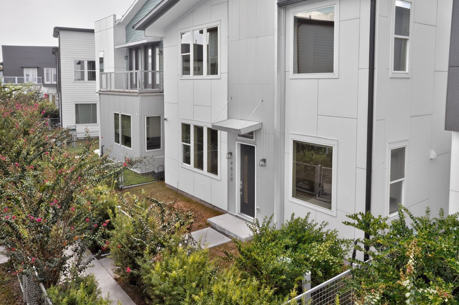Modern townhouse with sleek architecture, featuring large windows and a welcoming front entrance surrounded by lush greenery.