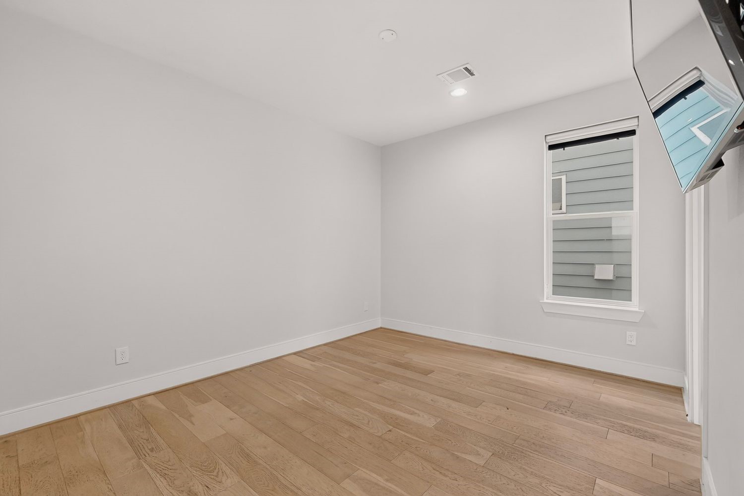 a vacant look at the bright and airy 2nd guest room featuring sleek hardwood floors, clean white walls, and a modern recessed lighting fixture, perfect for customization.